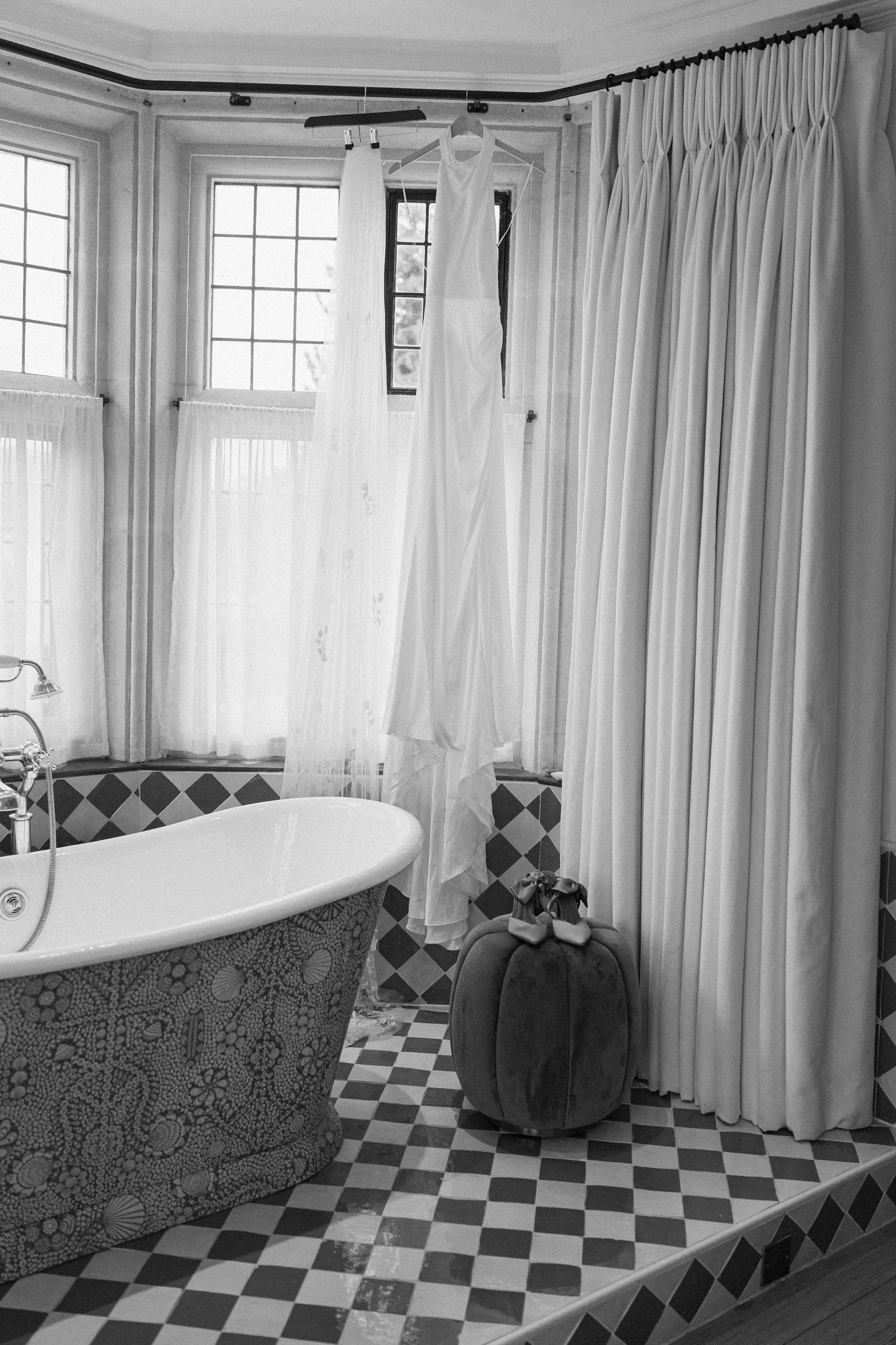 Wedding dress hanging in an elegant black and white tiled bathroom with a freestanding bathtub.