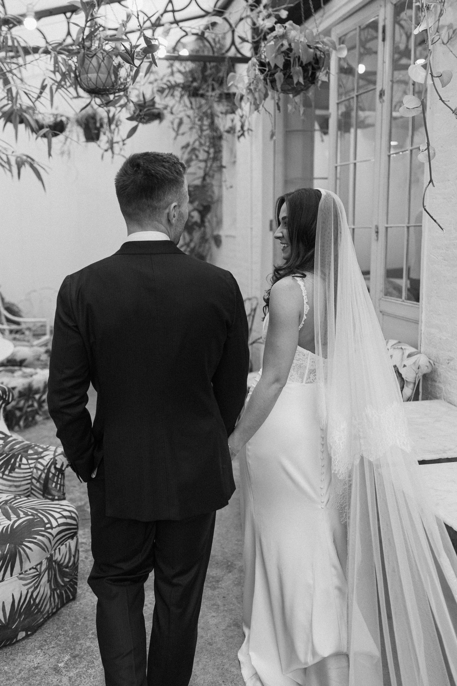 Bride and groom walk hand in hand in black and white wedding portrait outdoors.