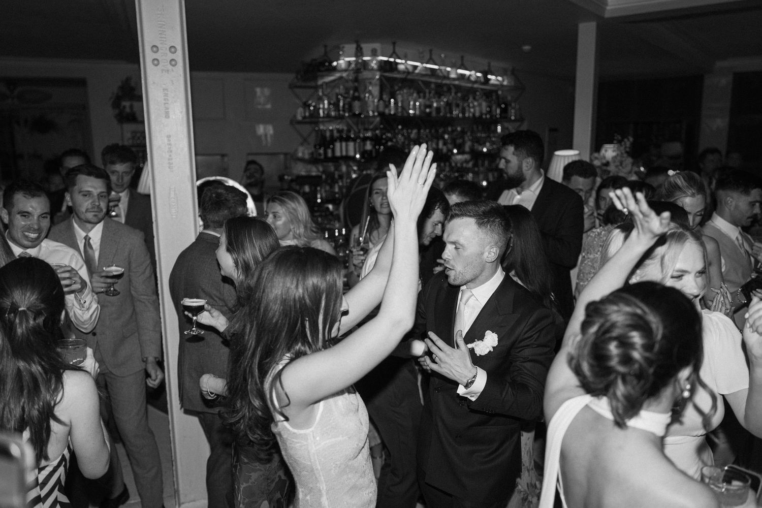 Black and white photo of wedding guests dancing and celebrating at a lively reception.