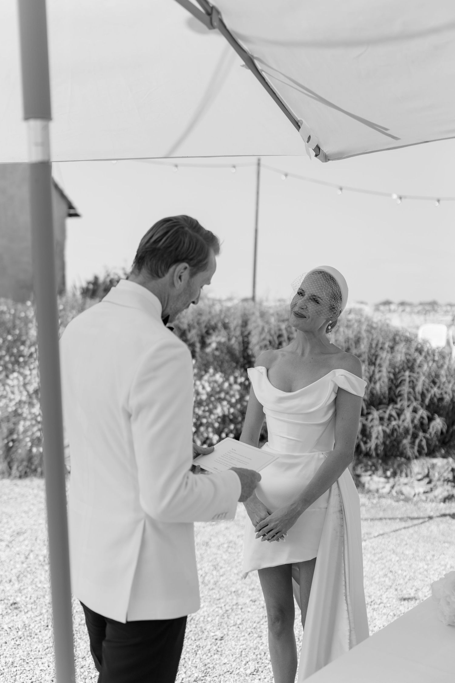 Black and white photo of a bride and groom exchanging vows at an outdoor wedding ceremony.