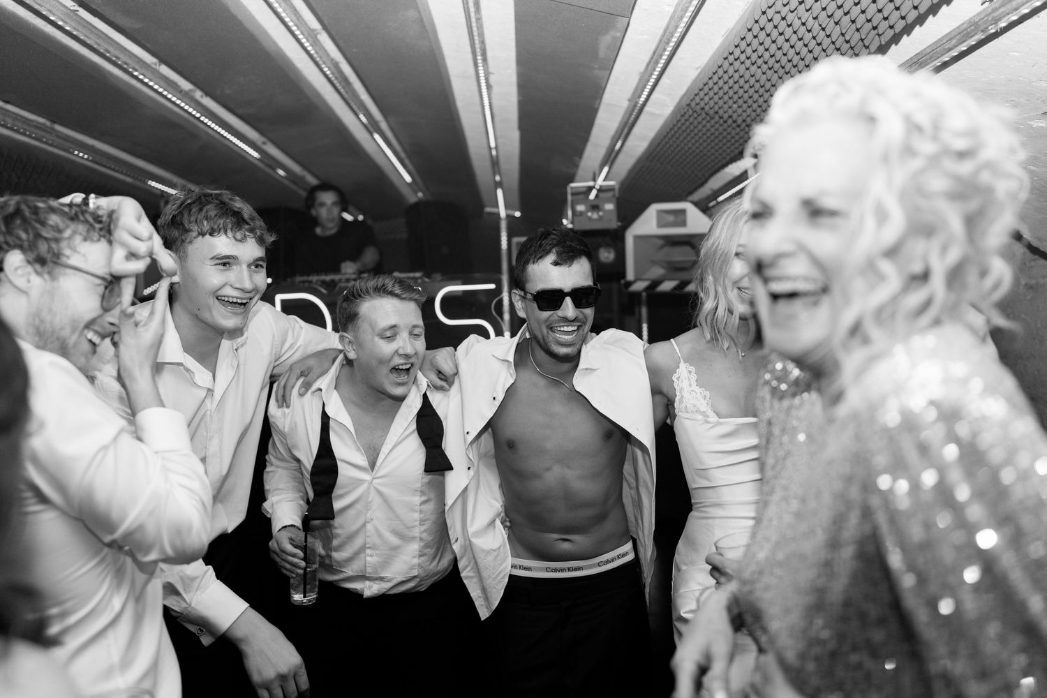Black and white photo of groom and guests laughing together at a fun wedding after-party.