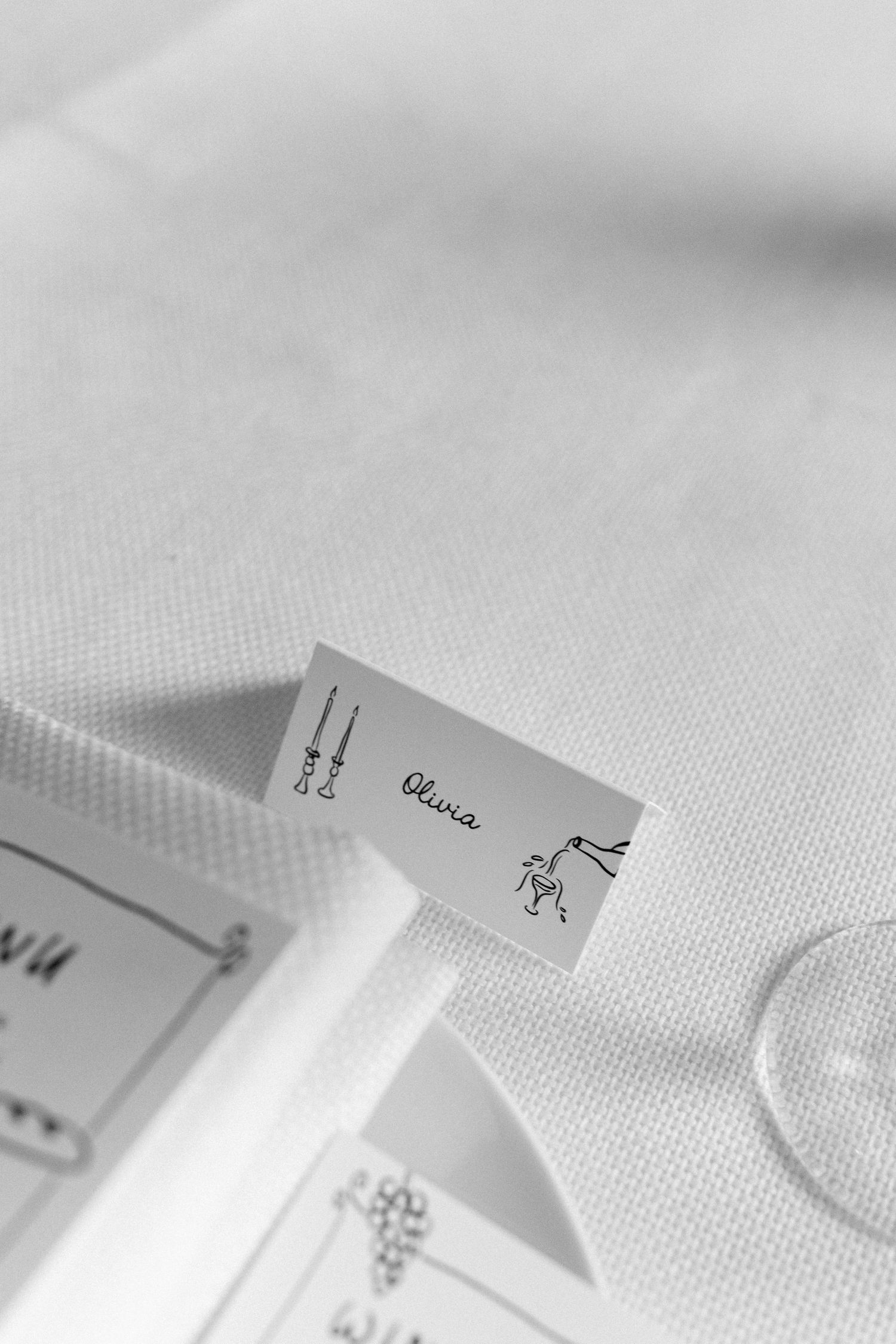 Black and white close-up of a wedding place card reading Olivia with decorative illustrations.