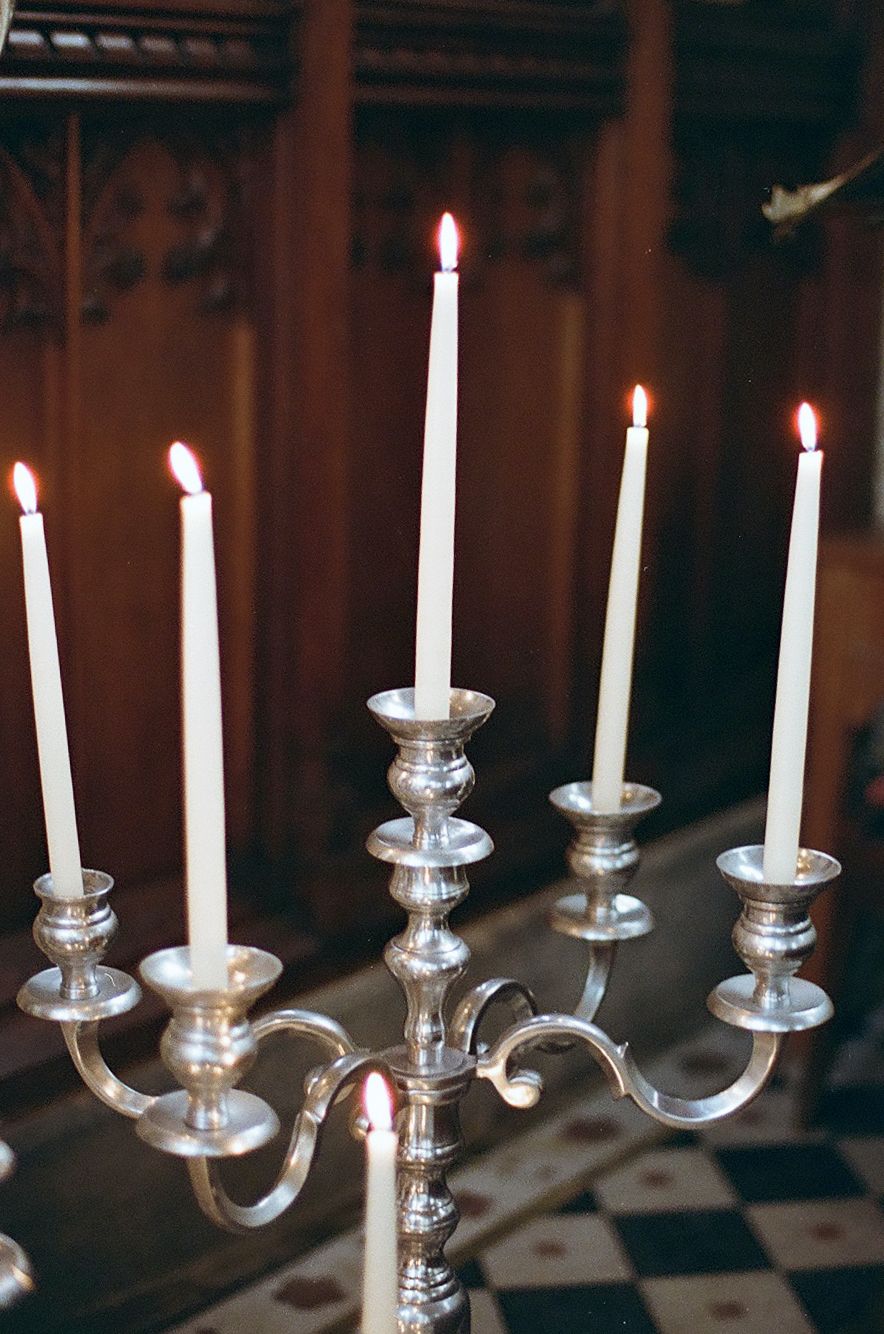 A row of elegant silver candelabras with white taper candles burning against a dark wooden background.