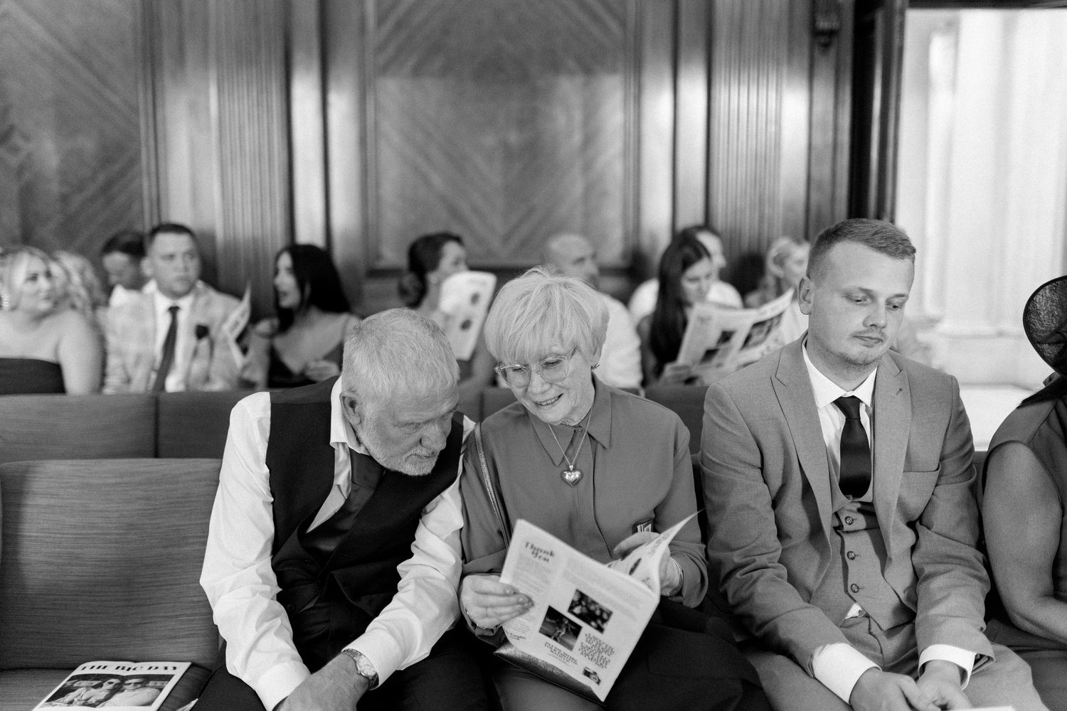 Wedding reception guests laughing and celebrating in wood-paneled venue.