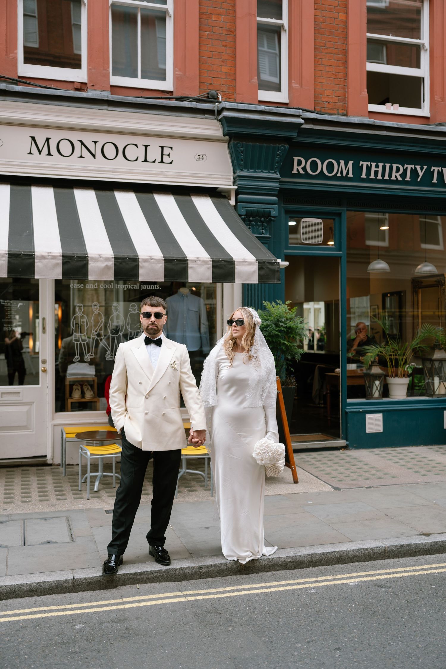 Couple walking past storefronts including Monocle shop in formal wedding attire.