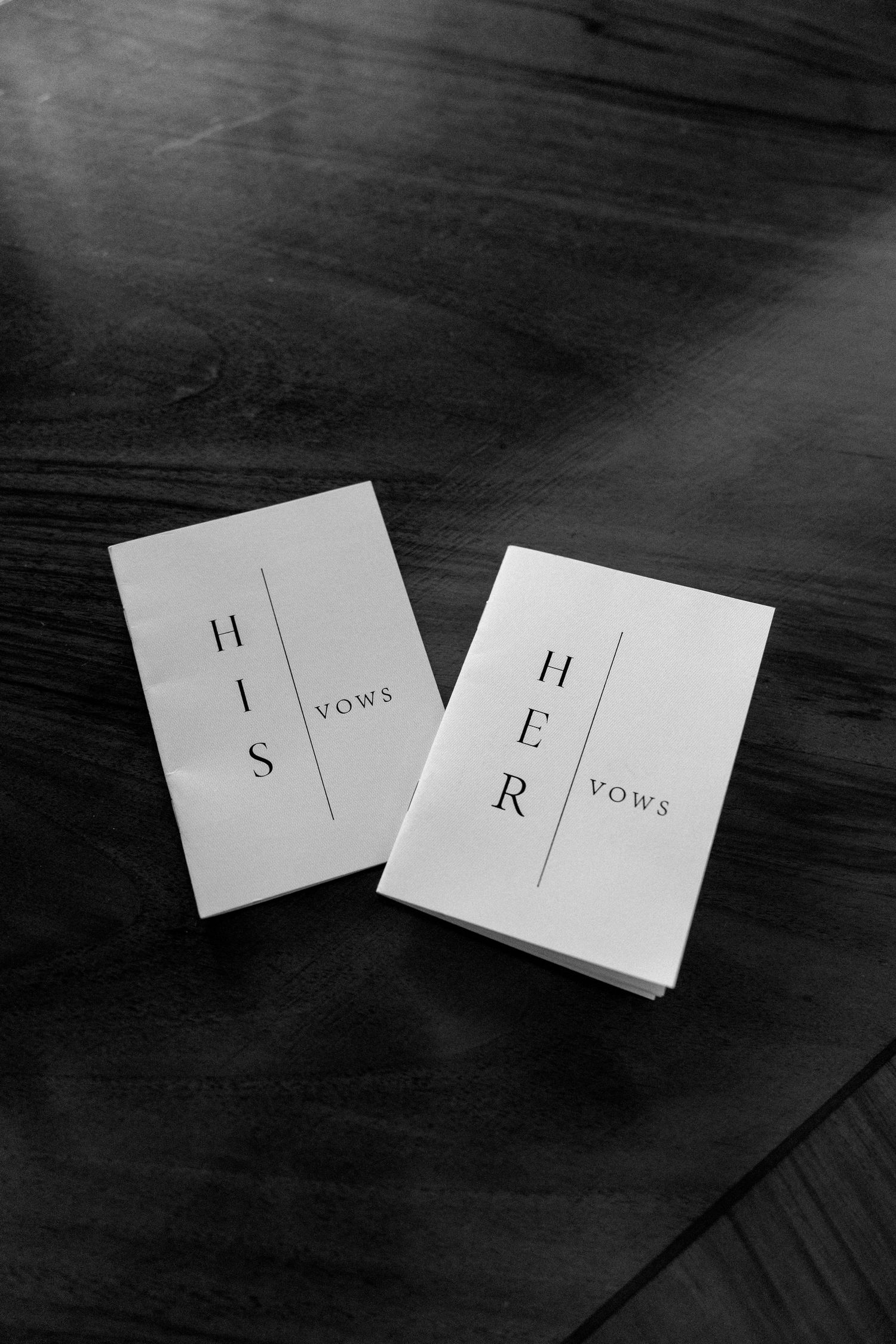 Two white vow books with minimalist design sit on a dark wooden surface.