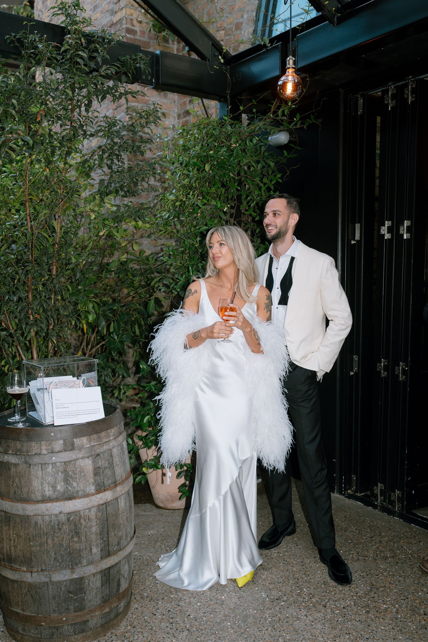 Dancing couple in white attire next to rustic wine barrels at an outdoor venue.