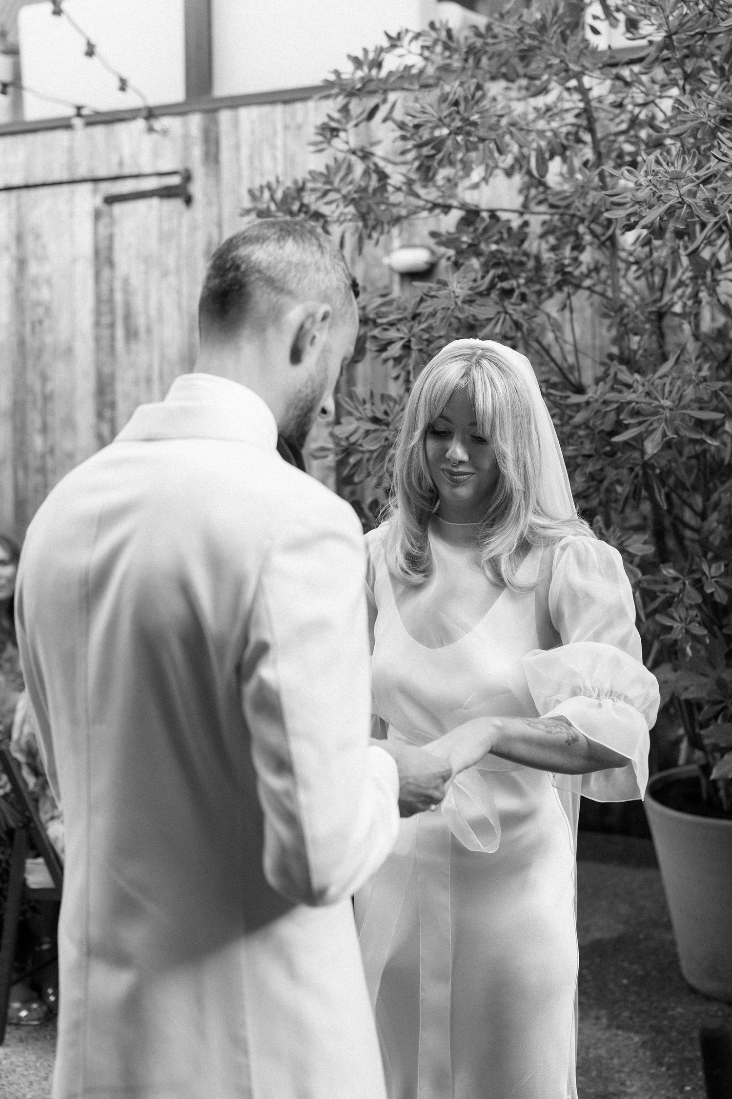 Couple in white formal attire embracing in a garden setting.