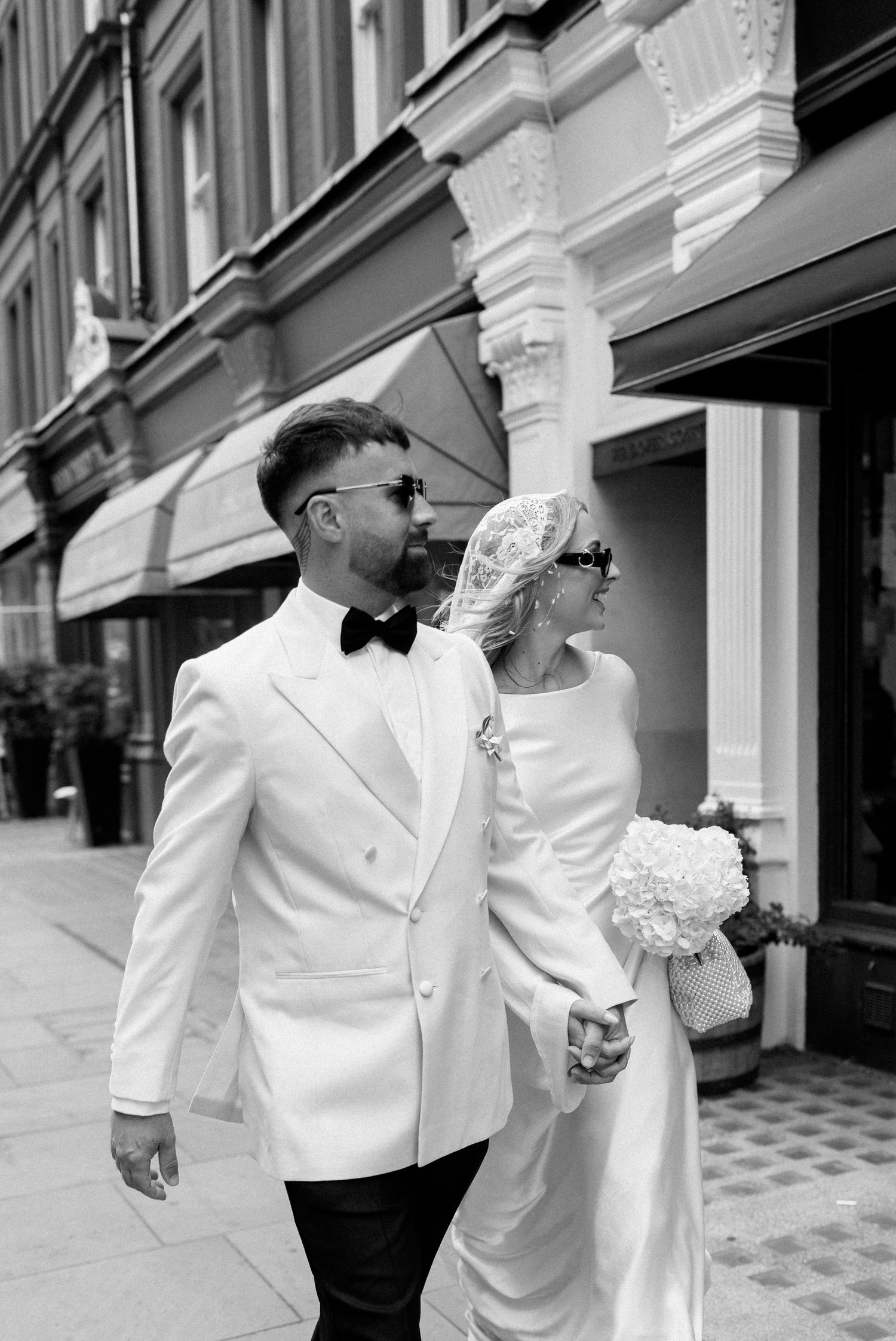Wedding couple walking along a street with classic architectural details and storefronts.