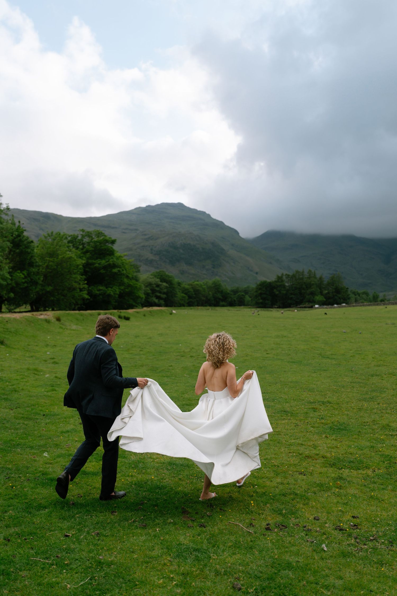 Couple walking through green field with misty mountains in the background.