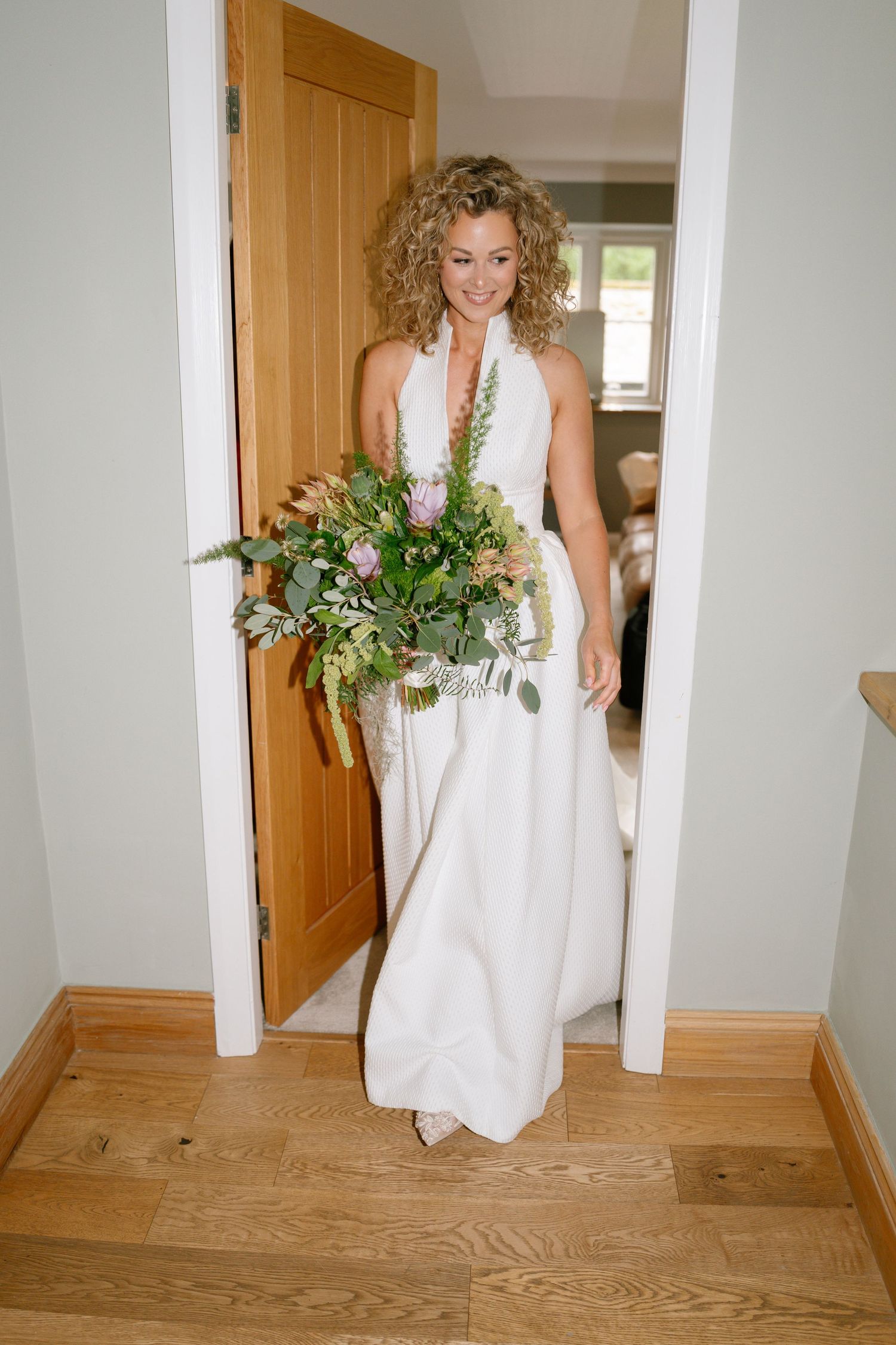 Person in flowing white wedding dress walking through hallway with wooden floors.