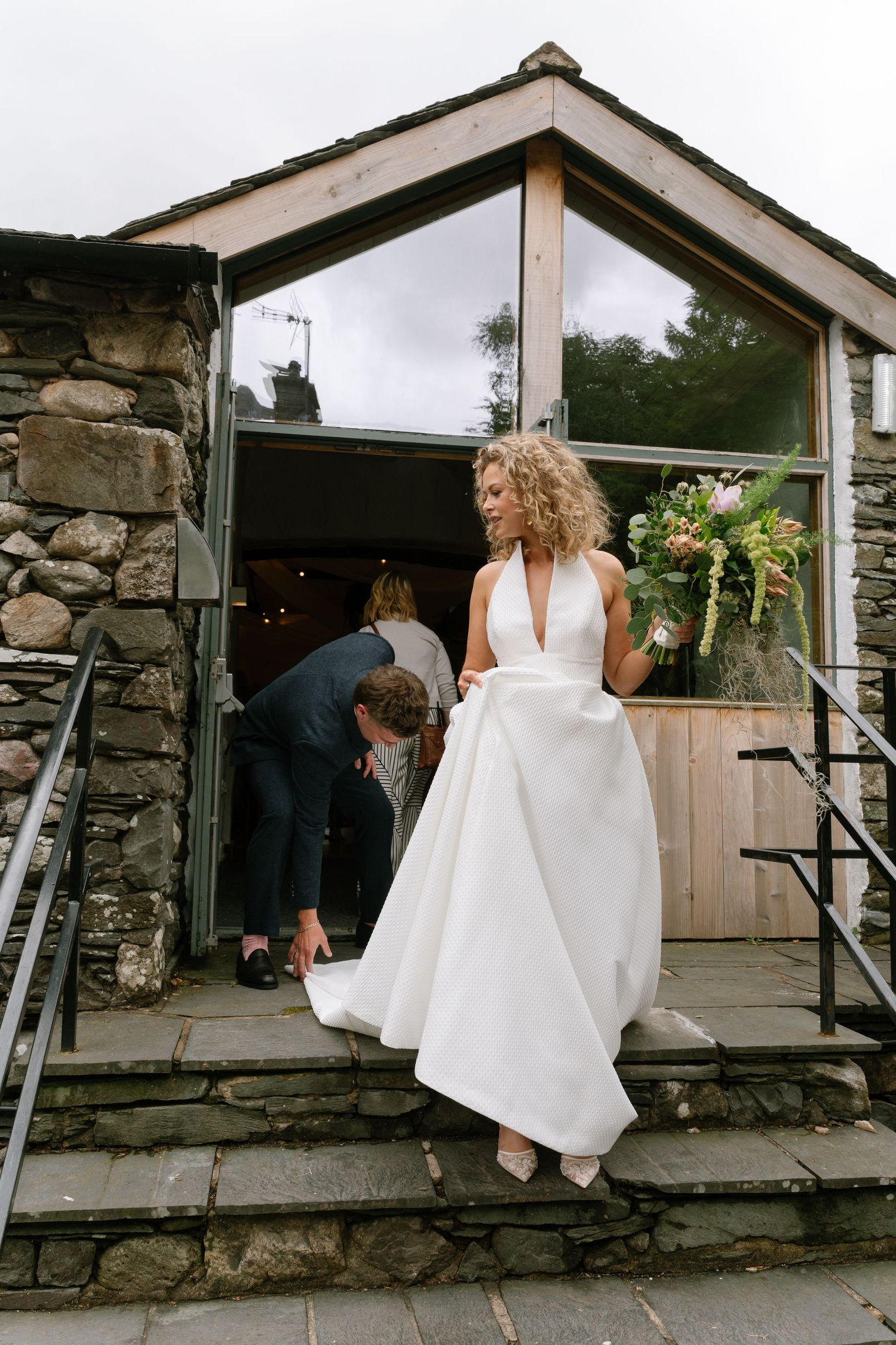 A bride in a white dress walks along a stone pathway at a rustic venue.