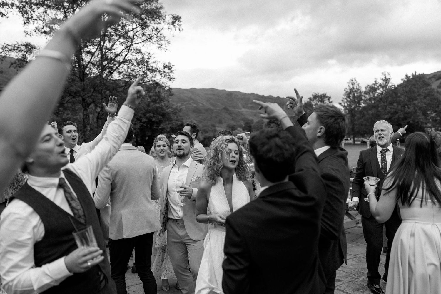 Wedding celebration with guests cheering and raising their hands in excitement outdoors.