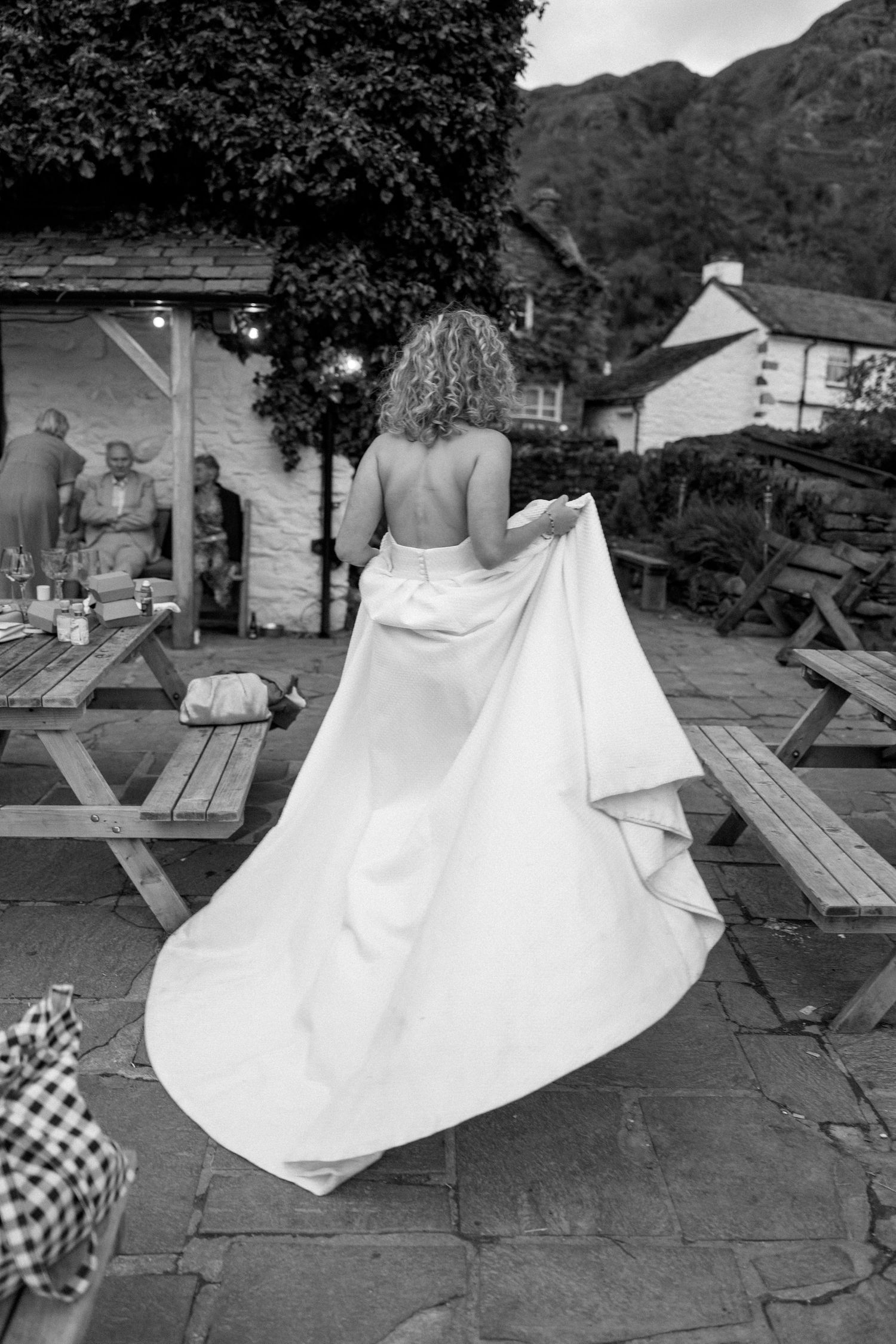 Back view of a bride in a flowing white dress standing on a stone patio with mountains in background.