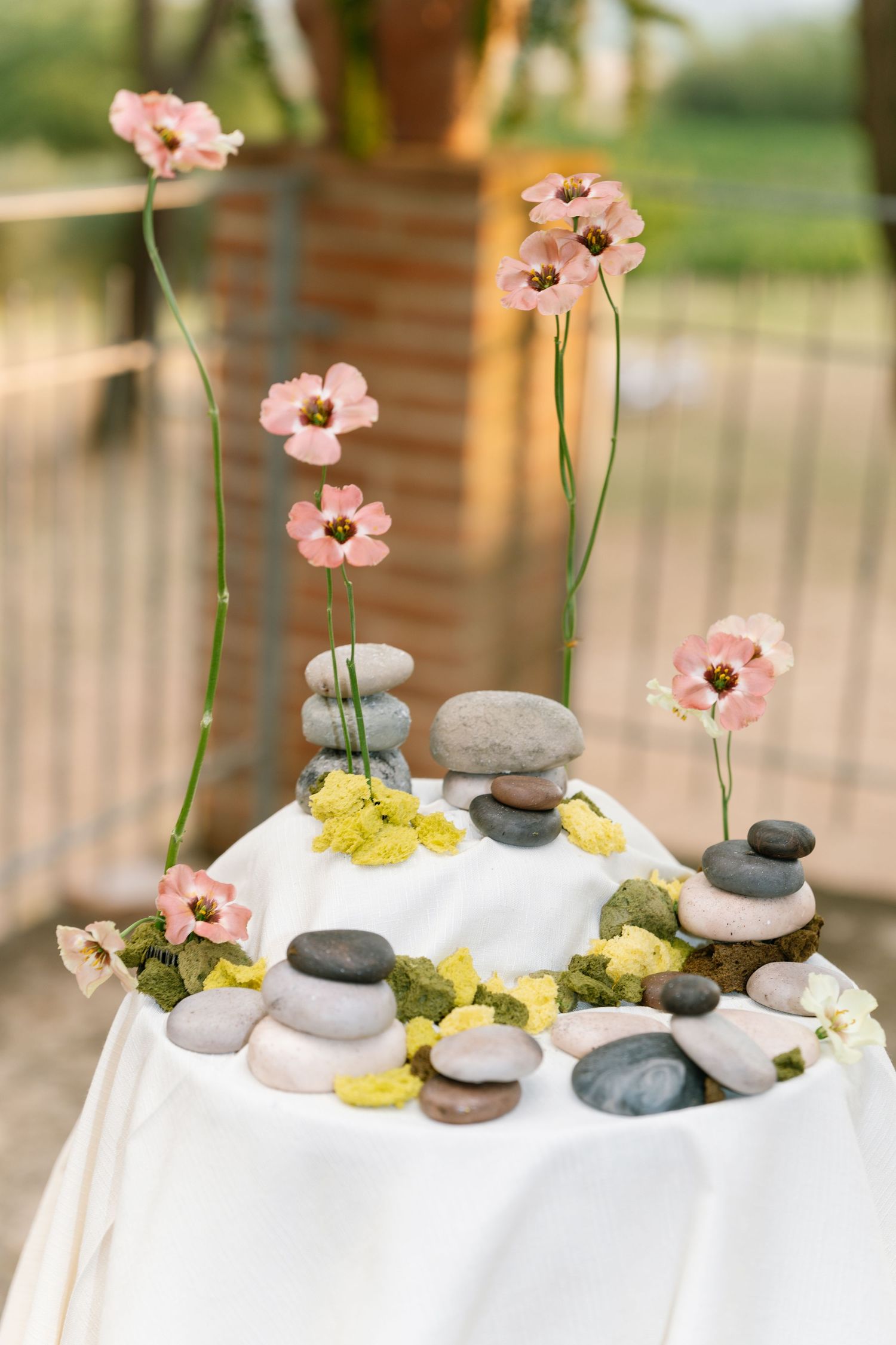 Decorative table display with pink flowers and smooth stones arranged on white linen.