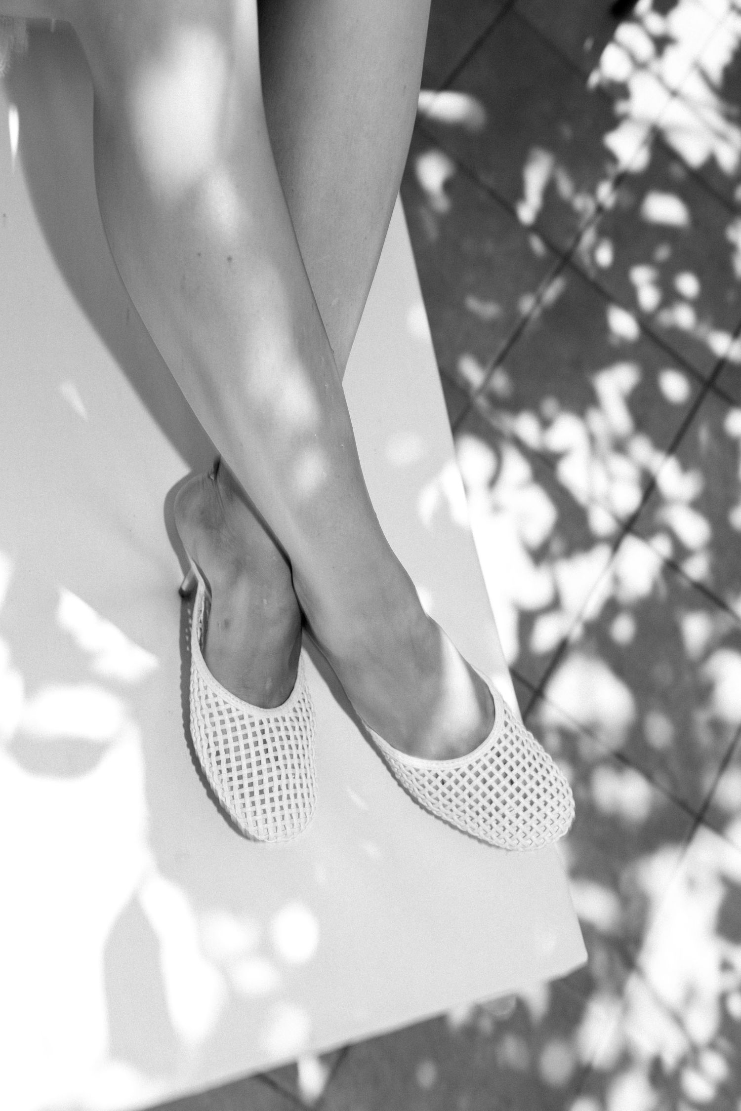 Close-up of feet wearing white perforated shoes with dappled sunlight shadows.