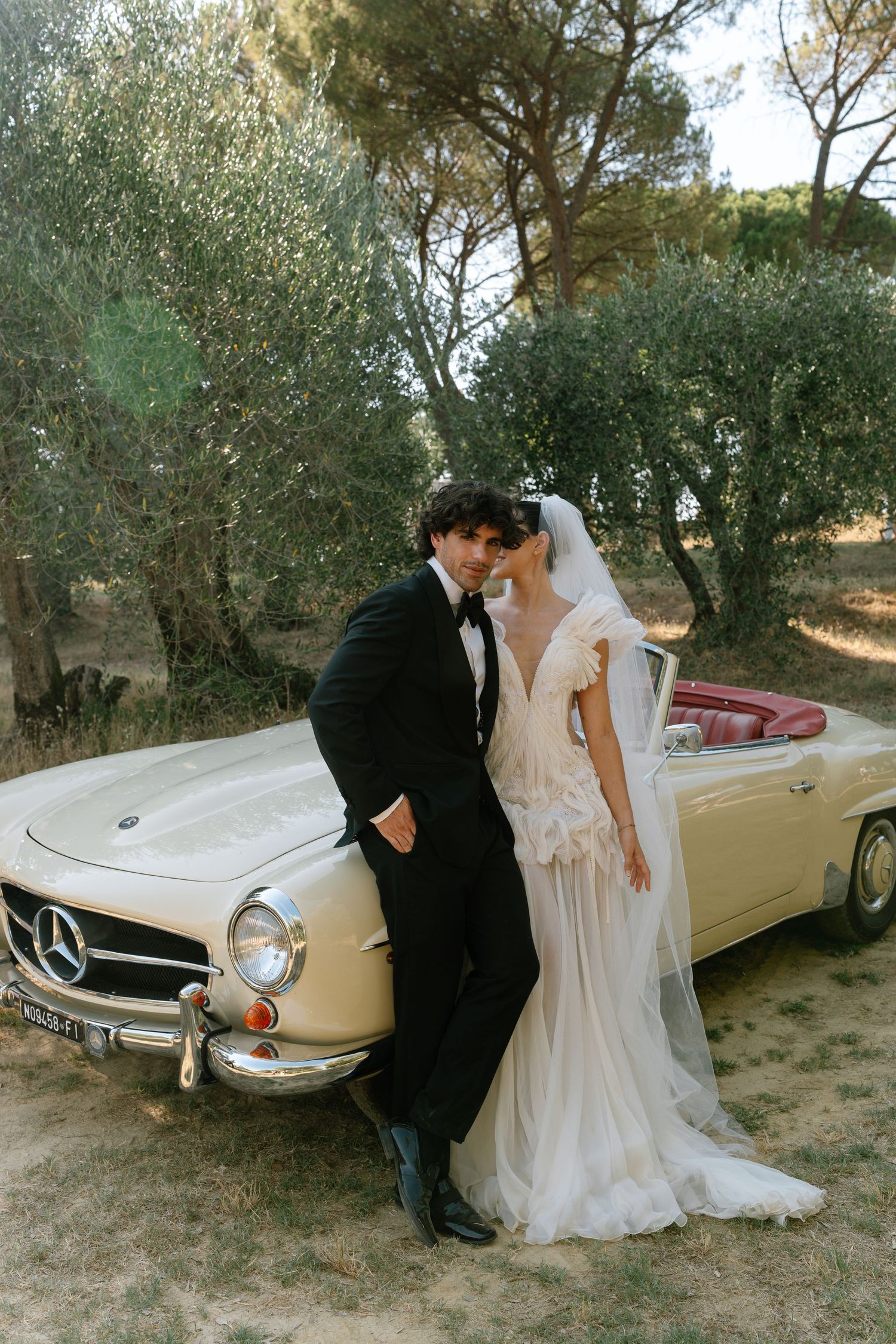 A romantic vintage car photoshoot in a rustic outdoor setting with a classic automobile and elegant attire.