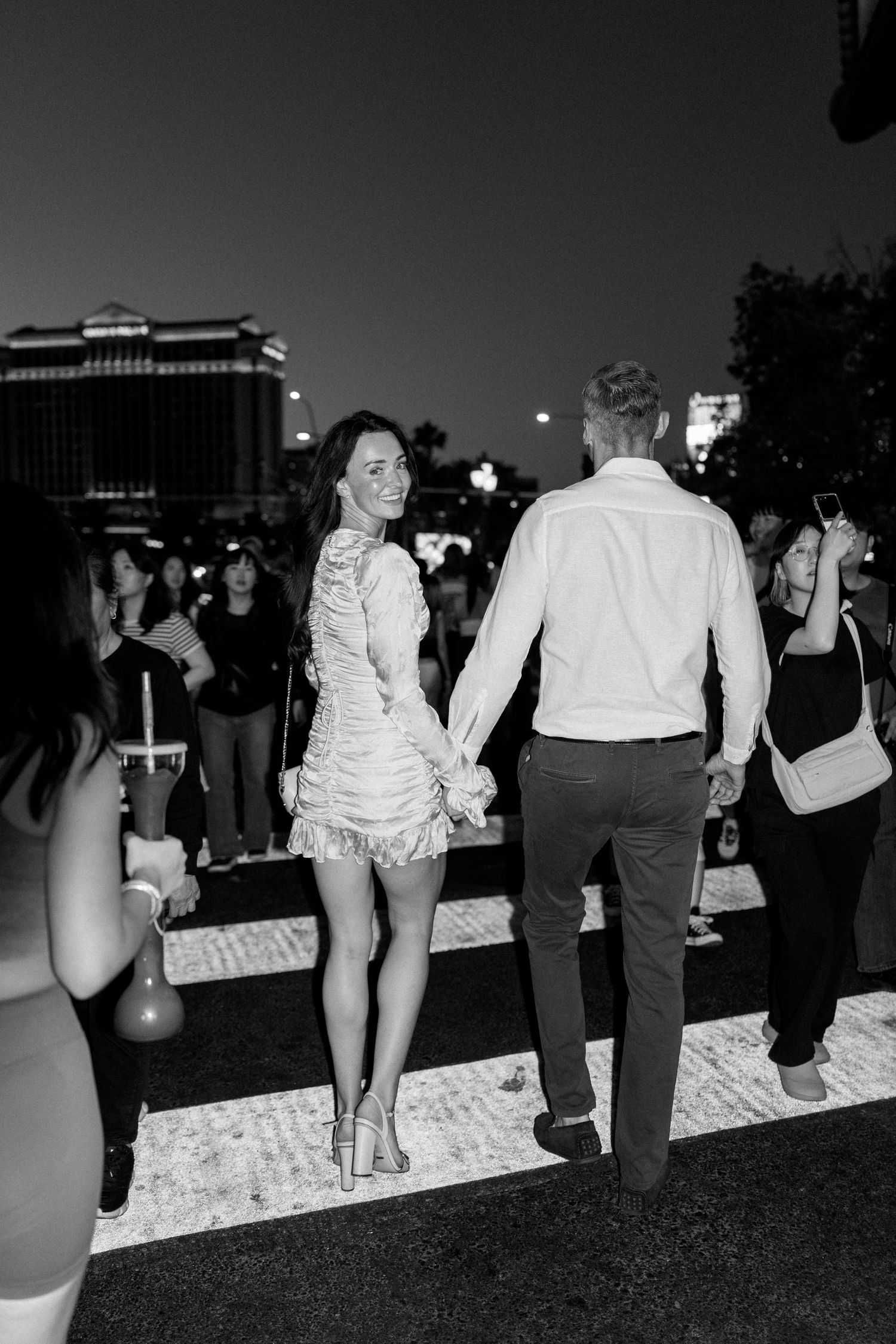 A black and white photo of a couple walking through a crowded Las Vegas street at night.