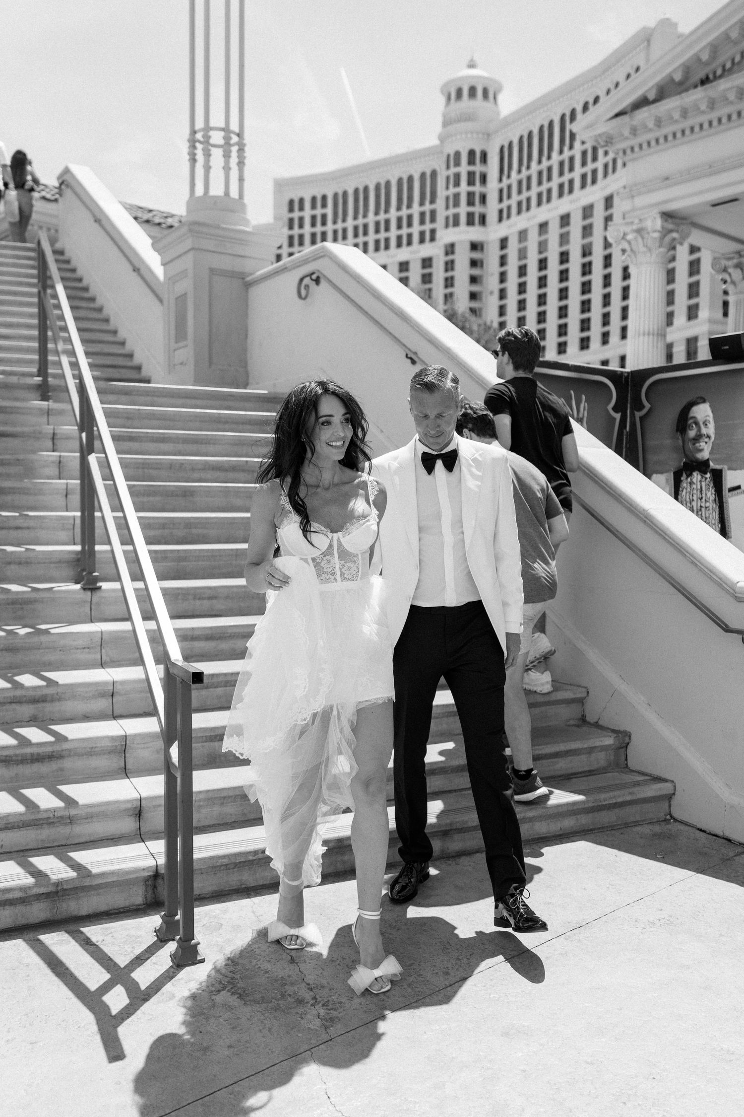 Couple in wedding attire poses on white steps with Las Vegas architecture in background.