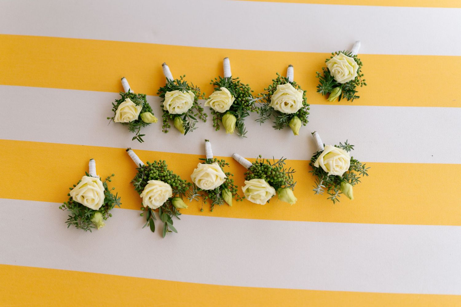 White roses and greenery arranged in decorative floral bouquets against yellow and white striped background.