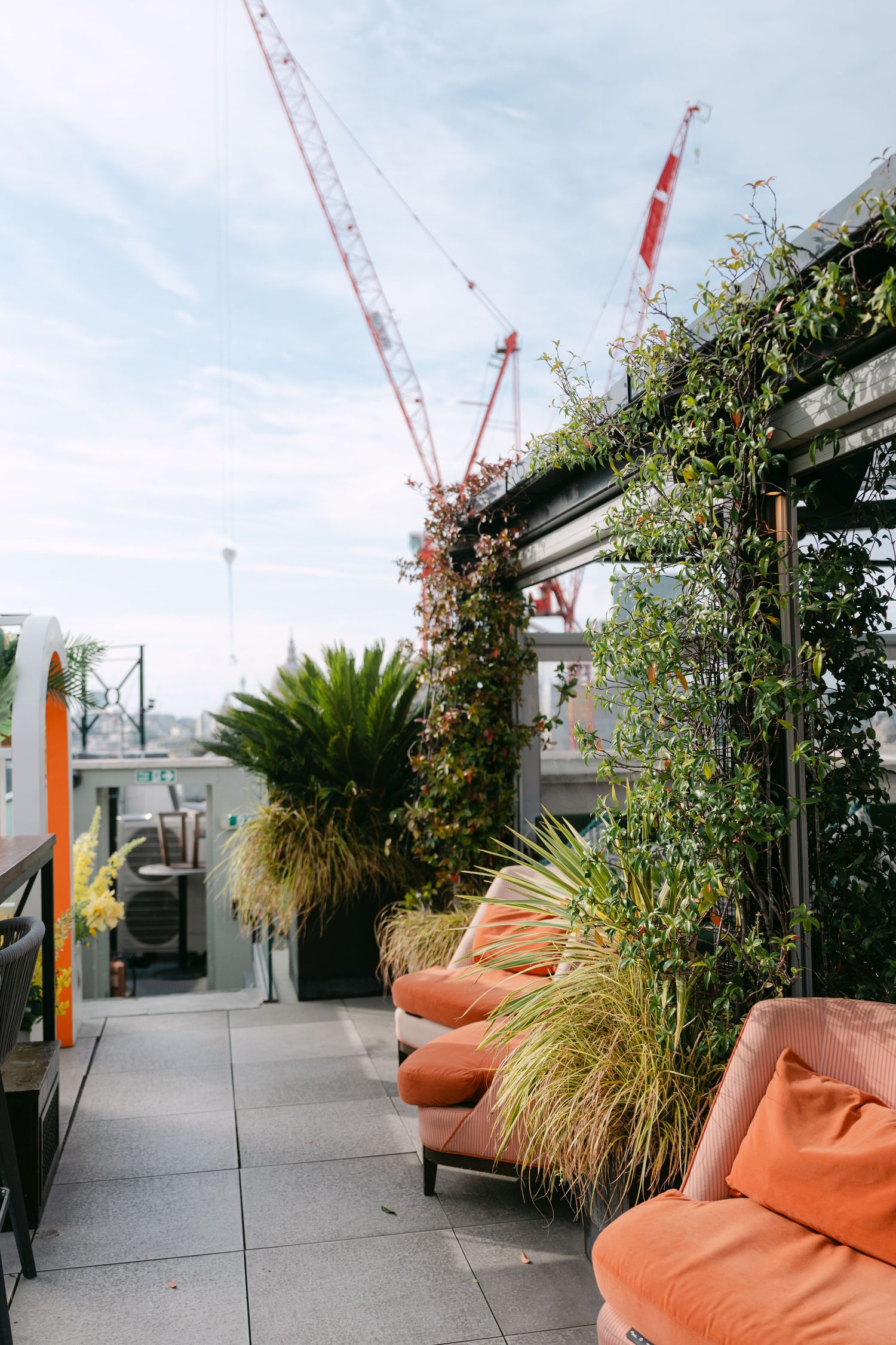Rooftop terrace with orange lounge chairs and construction cranes visible in distance.