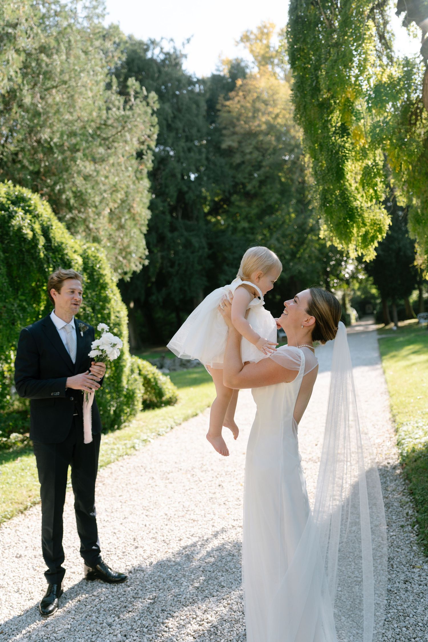 Wedding scene on garden path with couple and small child in white dress.