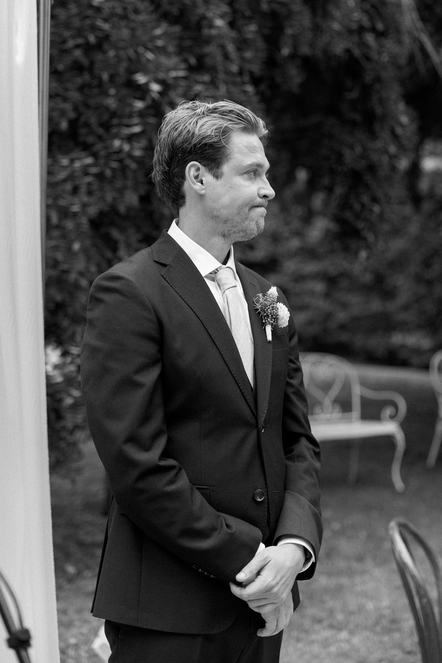 Groomsmen in black suits stand together under a white gazebo during a wedding ceremony.