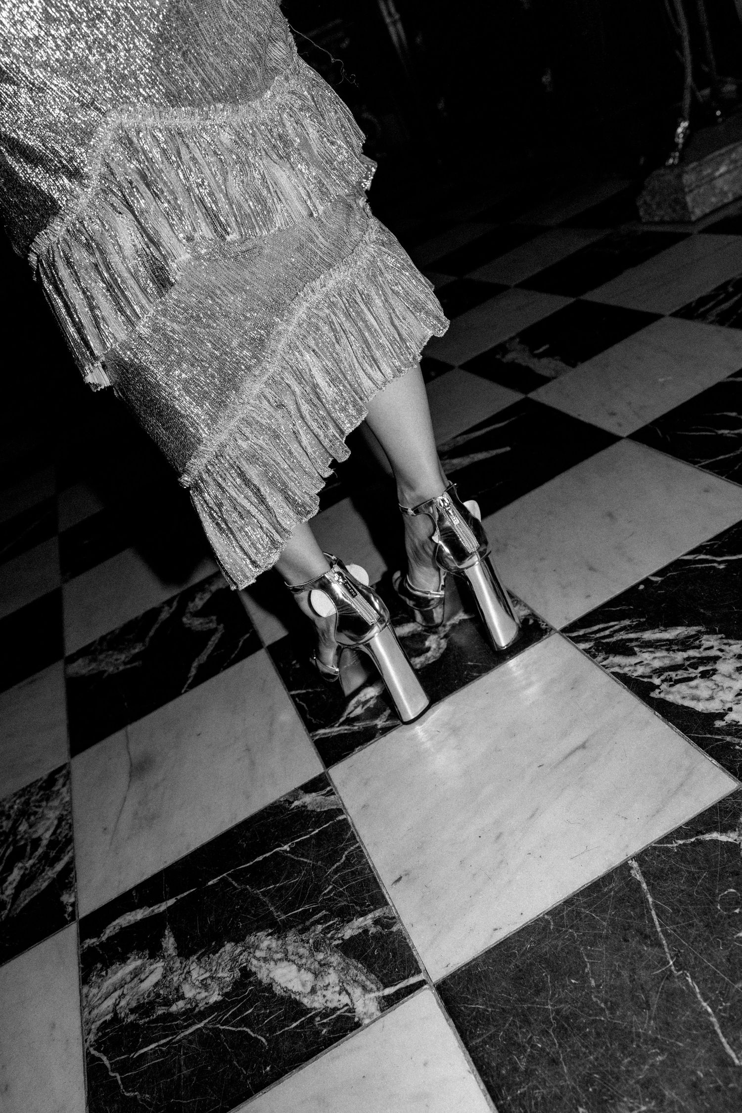 Close-up shots of silver heels moving across black and white marble tiles.