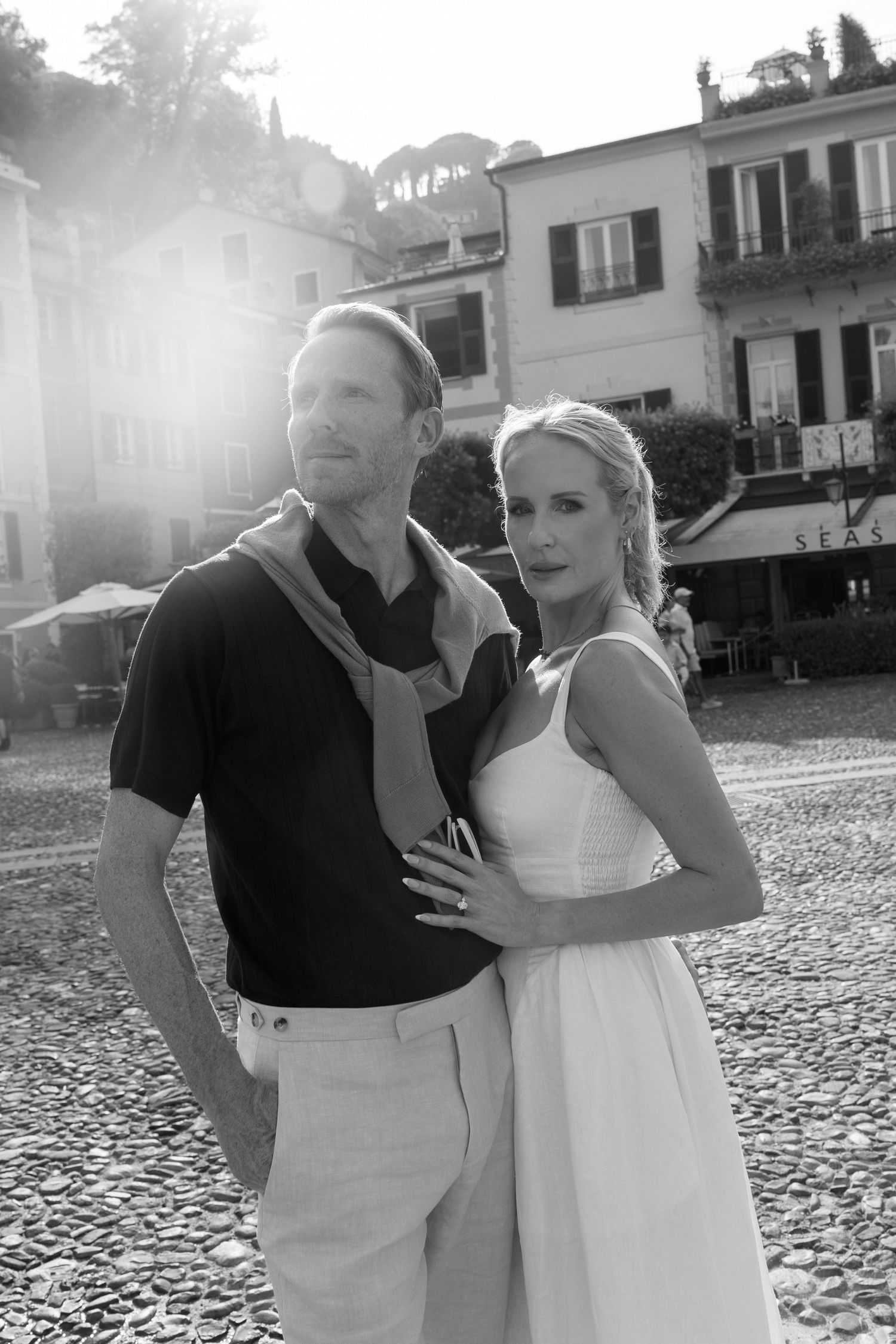 Black and white photo of elegant couple posing in Italian piazza with cobblestone street and historic buildings.