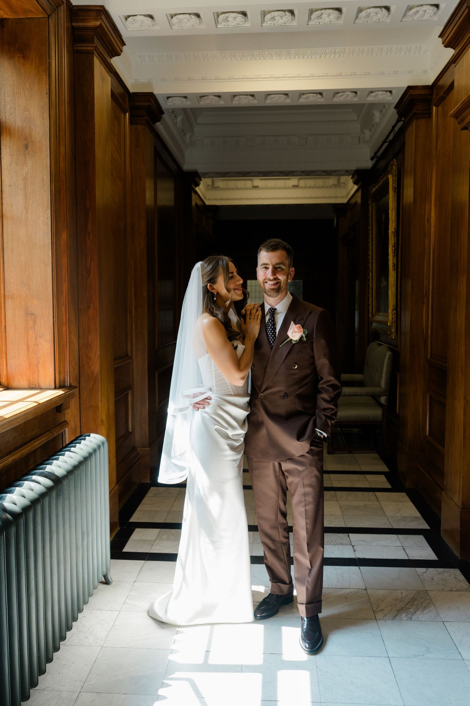Bride and groom posing in an elegant wood-paneled hallway with checkered floors at their wedding.