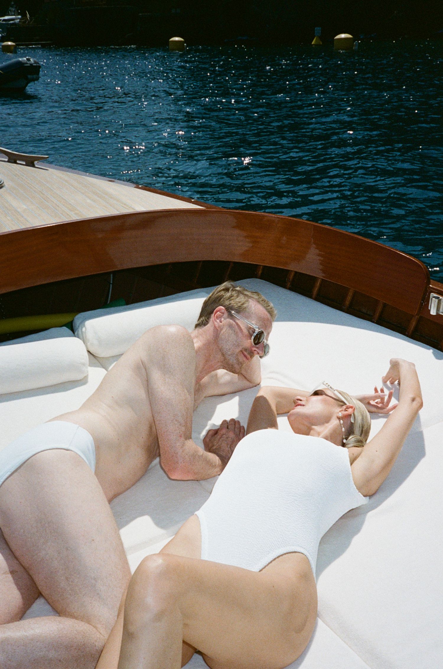 Couple in matching white swimwear relaxing and laughing together on the sun deck of a luxury yacht.