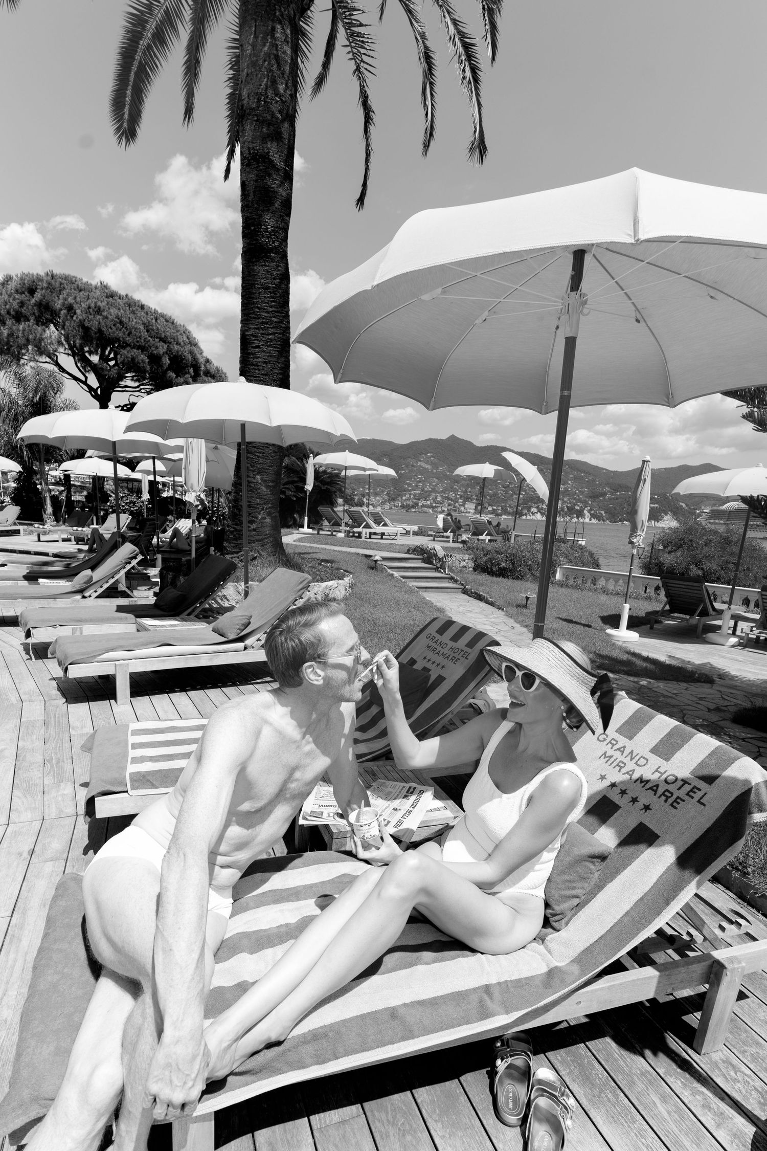 Couple relaxing on sun loungers under white umbrellas at a luxury Italian beach club, black and white.