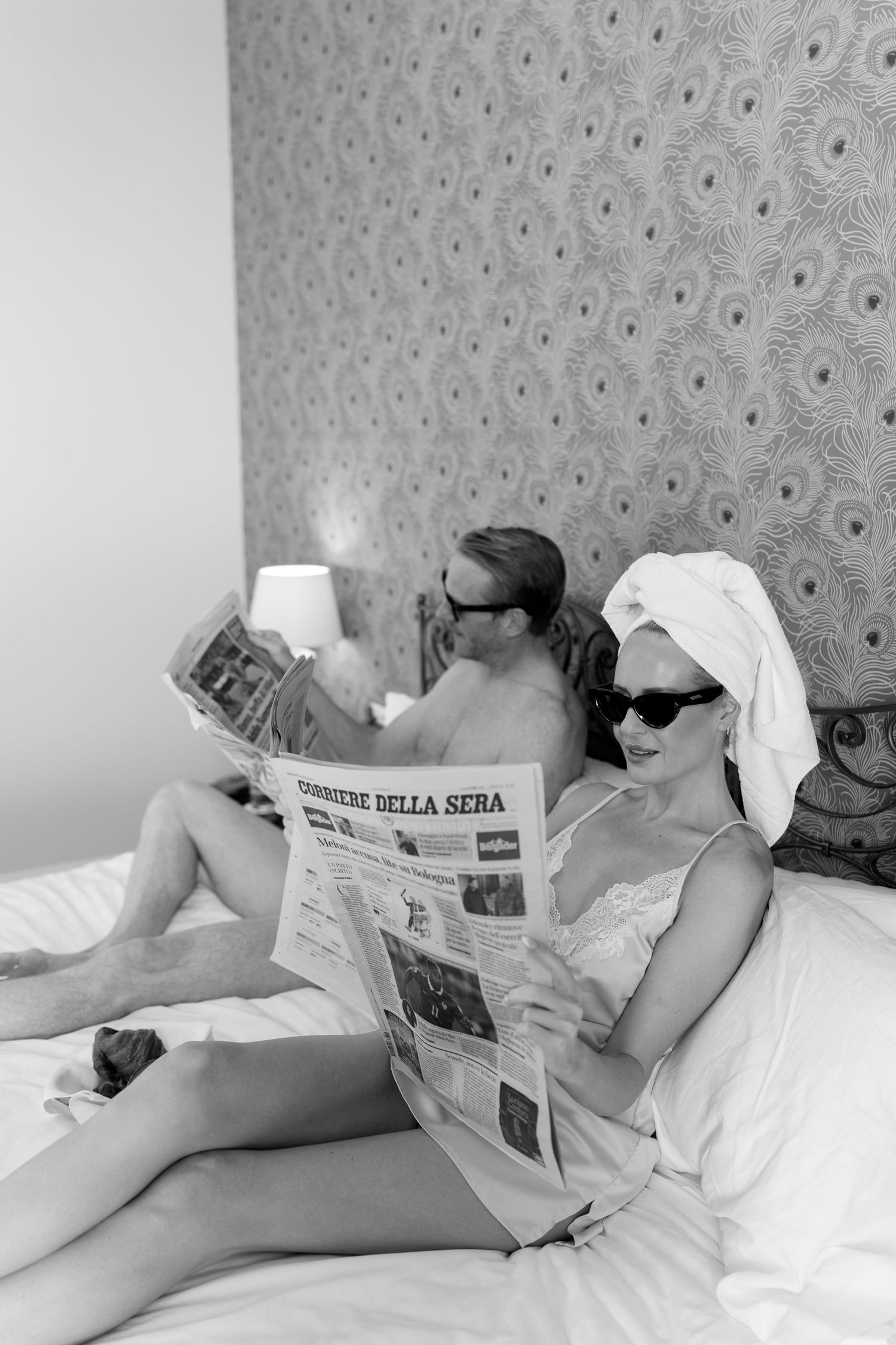 Black and white photo of couple reading Italian newspapers in bed at luxury hotel room.