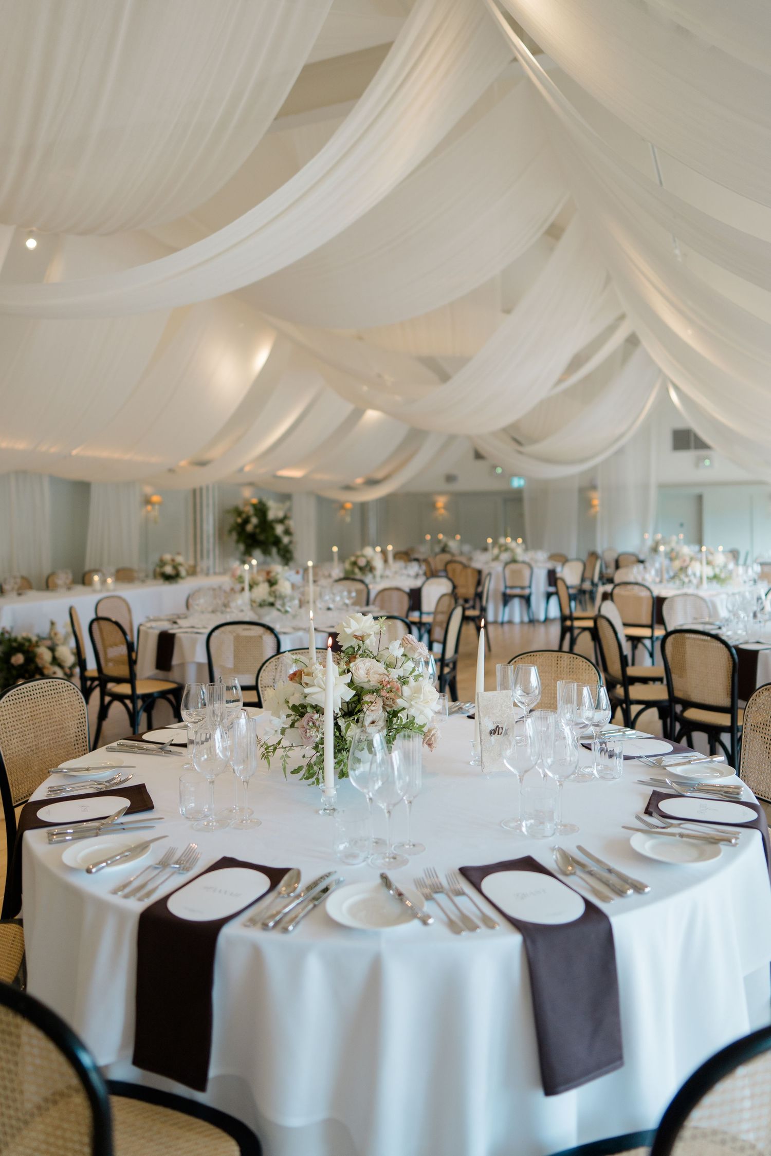 Elegant wedding reception hall with white draped ceiling, round tables and floral centerpieces.