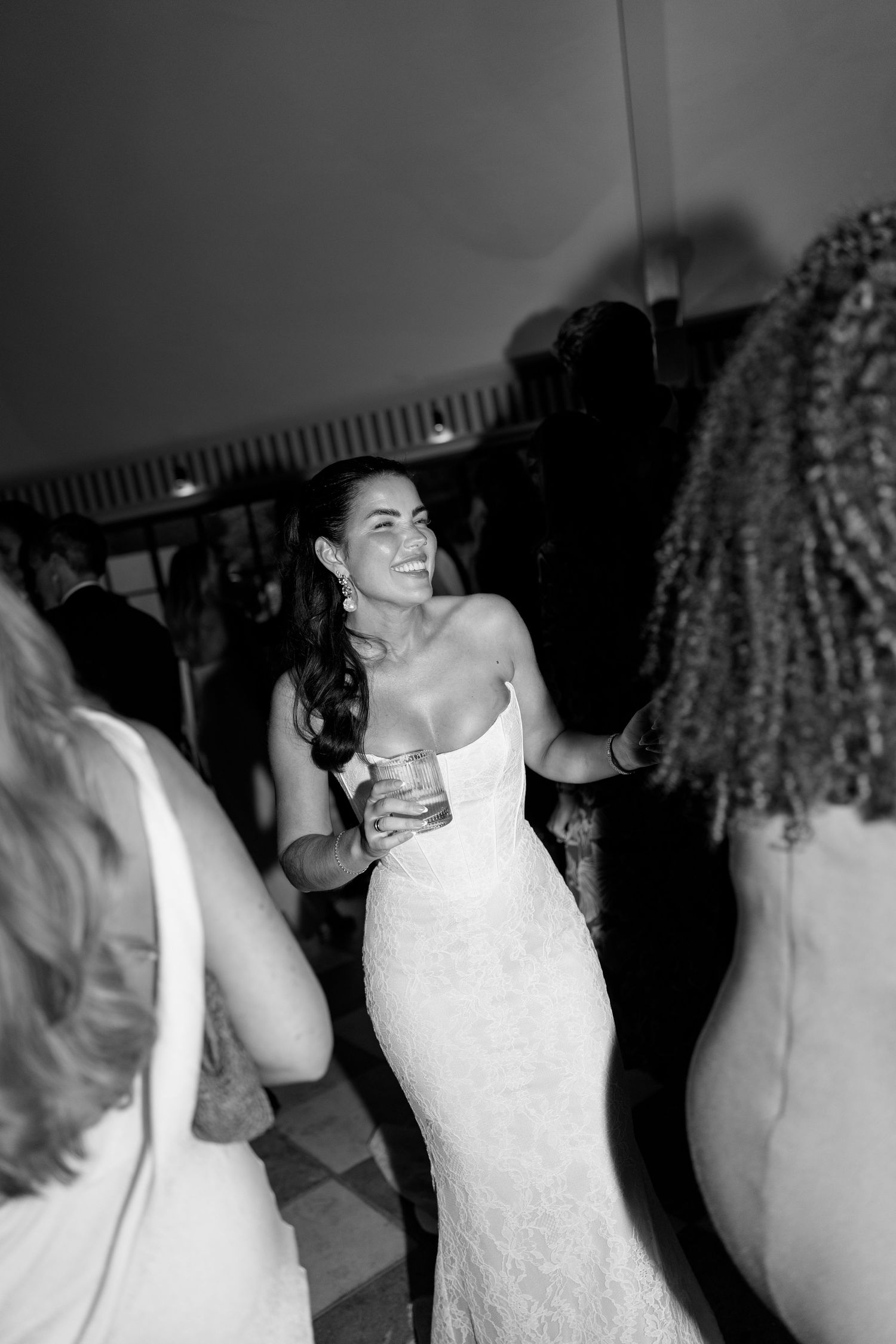 Black and white photo of radiant bride in strapless lace gown dancing joyfully at wedding reception.