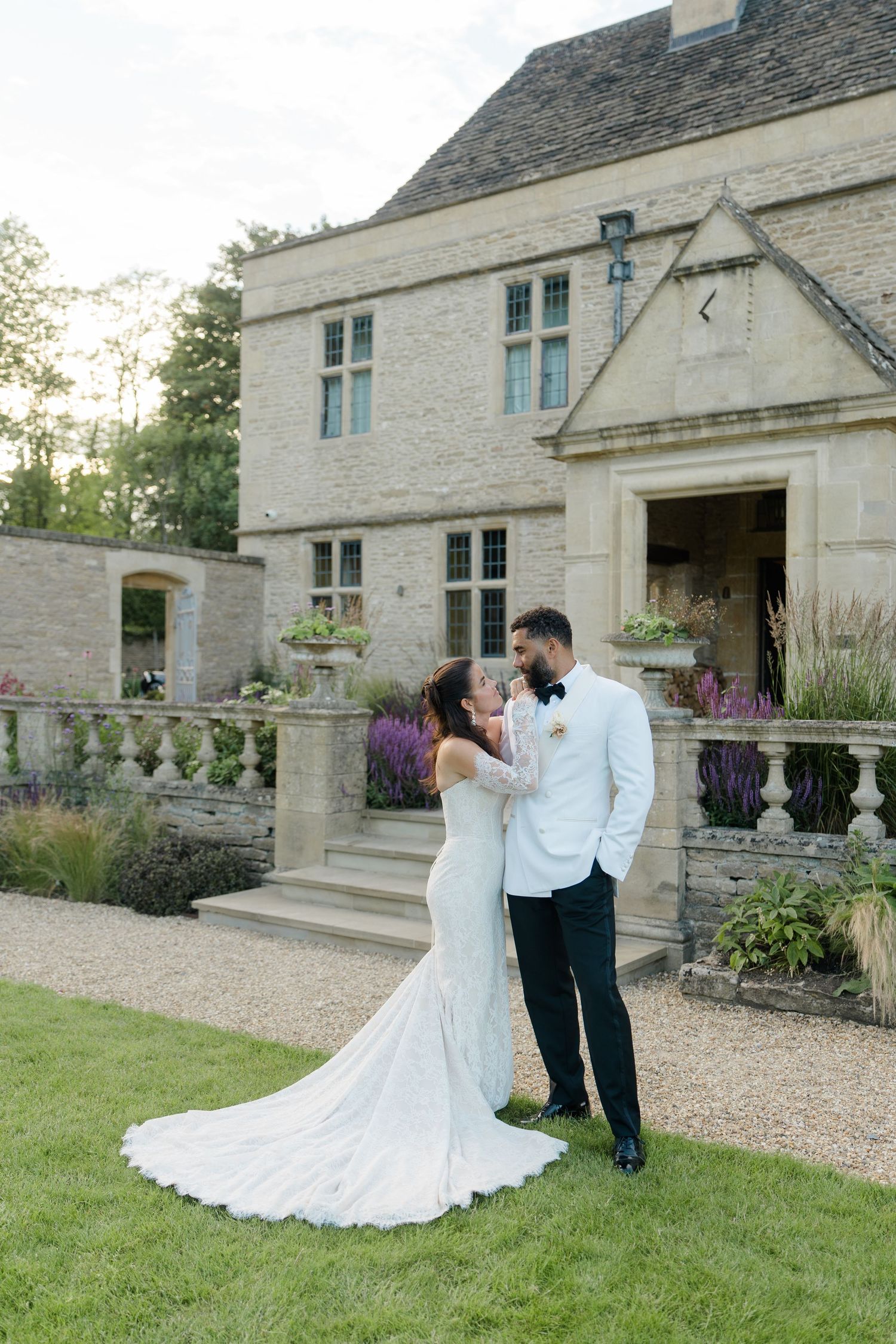 Bride and groom sharing a romantic moment at dusk outside an elegant stone English country manor house.