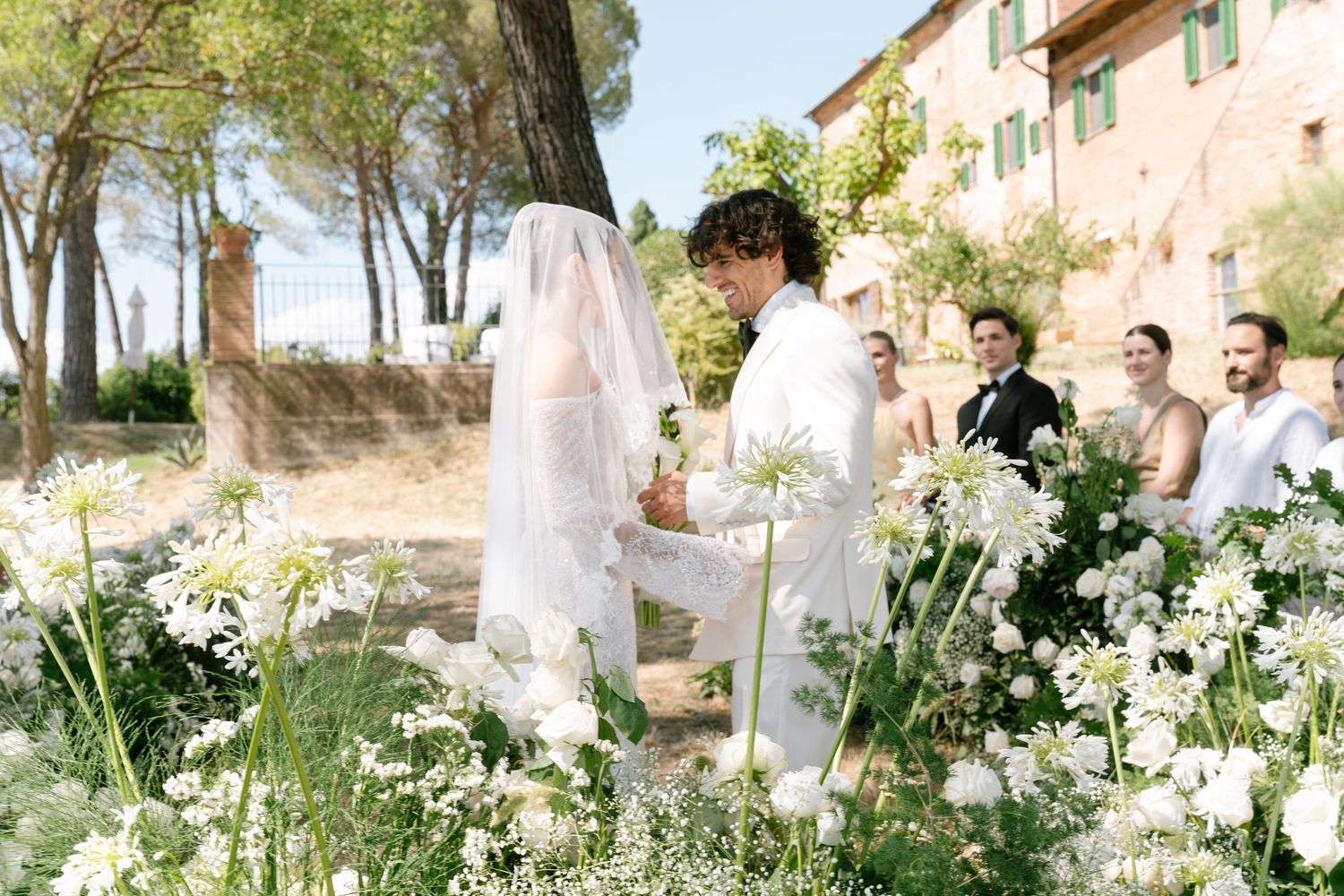 Elegant outdoor wedding ceremony setup with white floral arrangements and natural greenery in a garden setting.