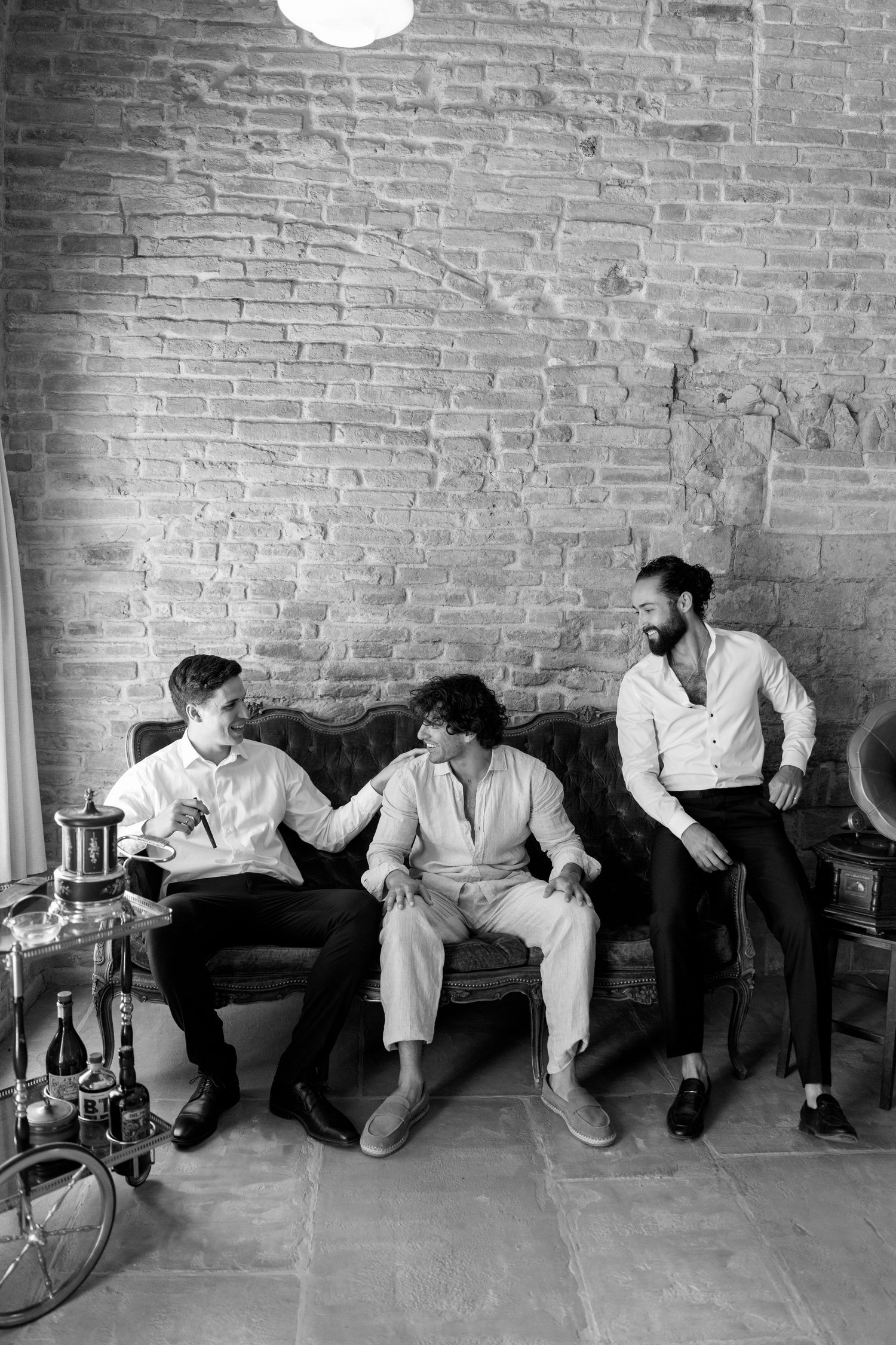 Three people sitting on a couch against a brick wall in a black and white casual setting.