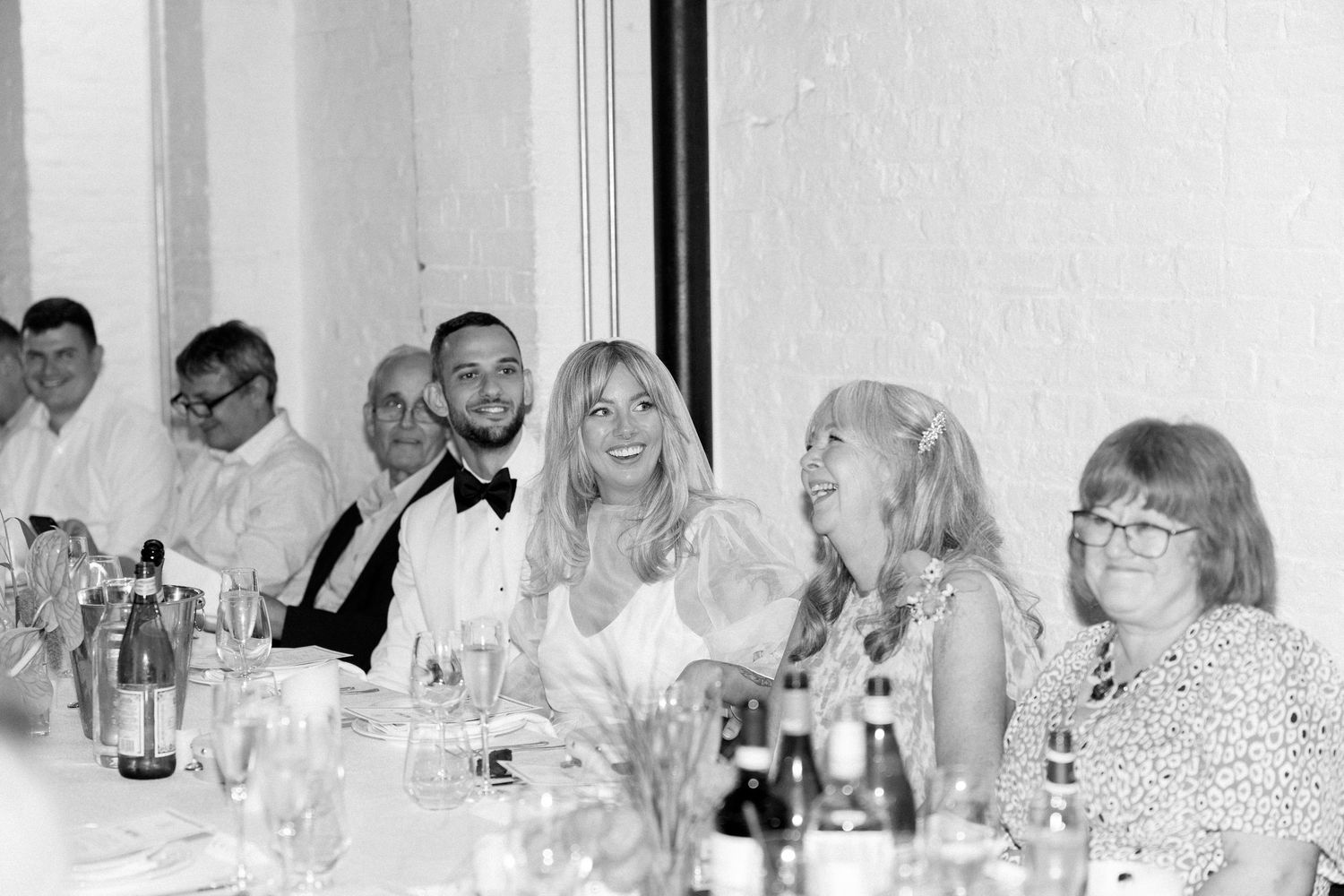 Wedding guests seated at long tables during reception dinner in modern white venue.