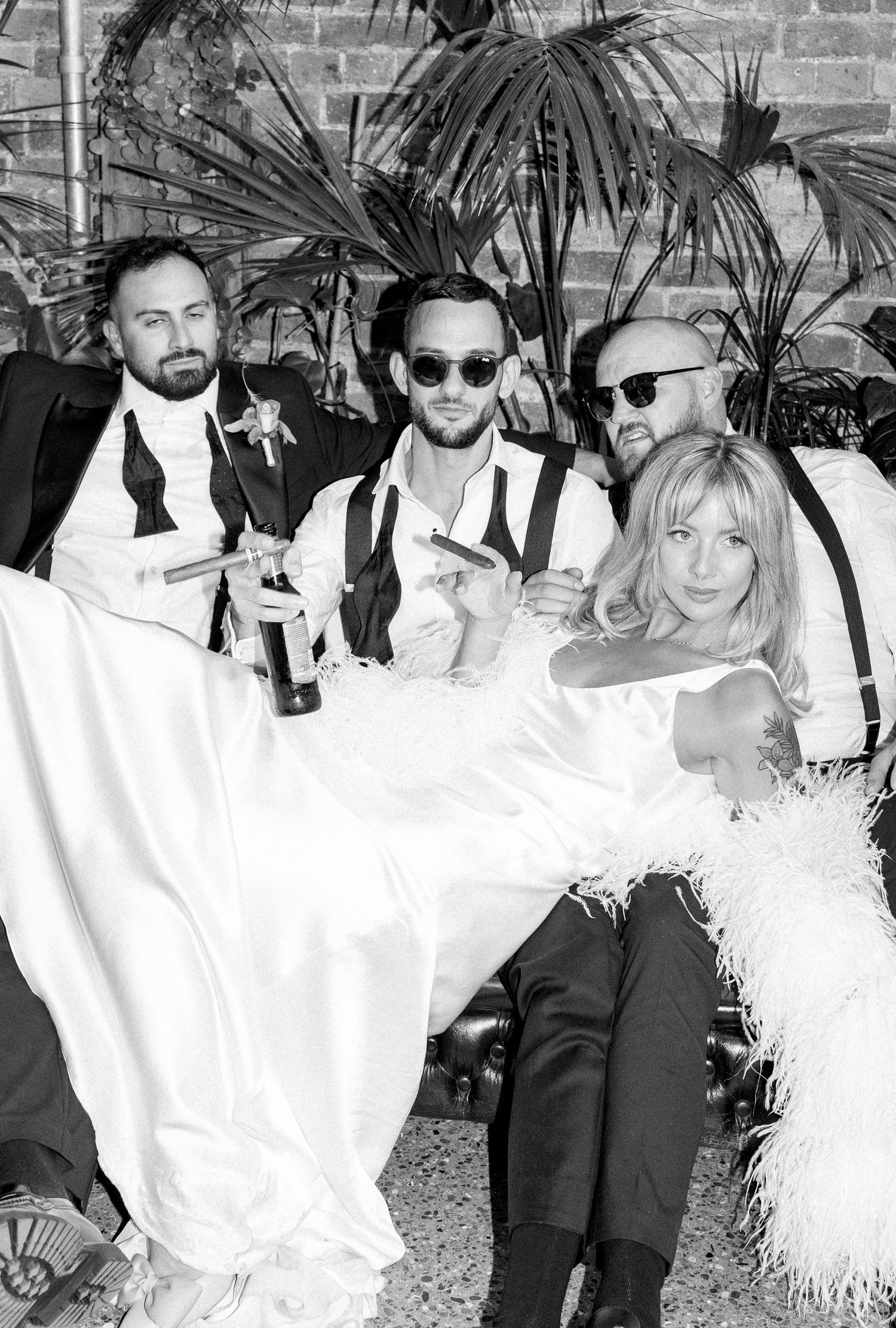 Wedding party in black and white attire posing with sunglasses and tropical decor.