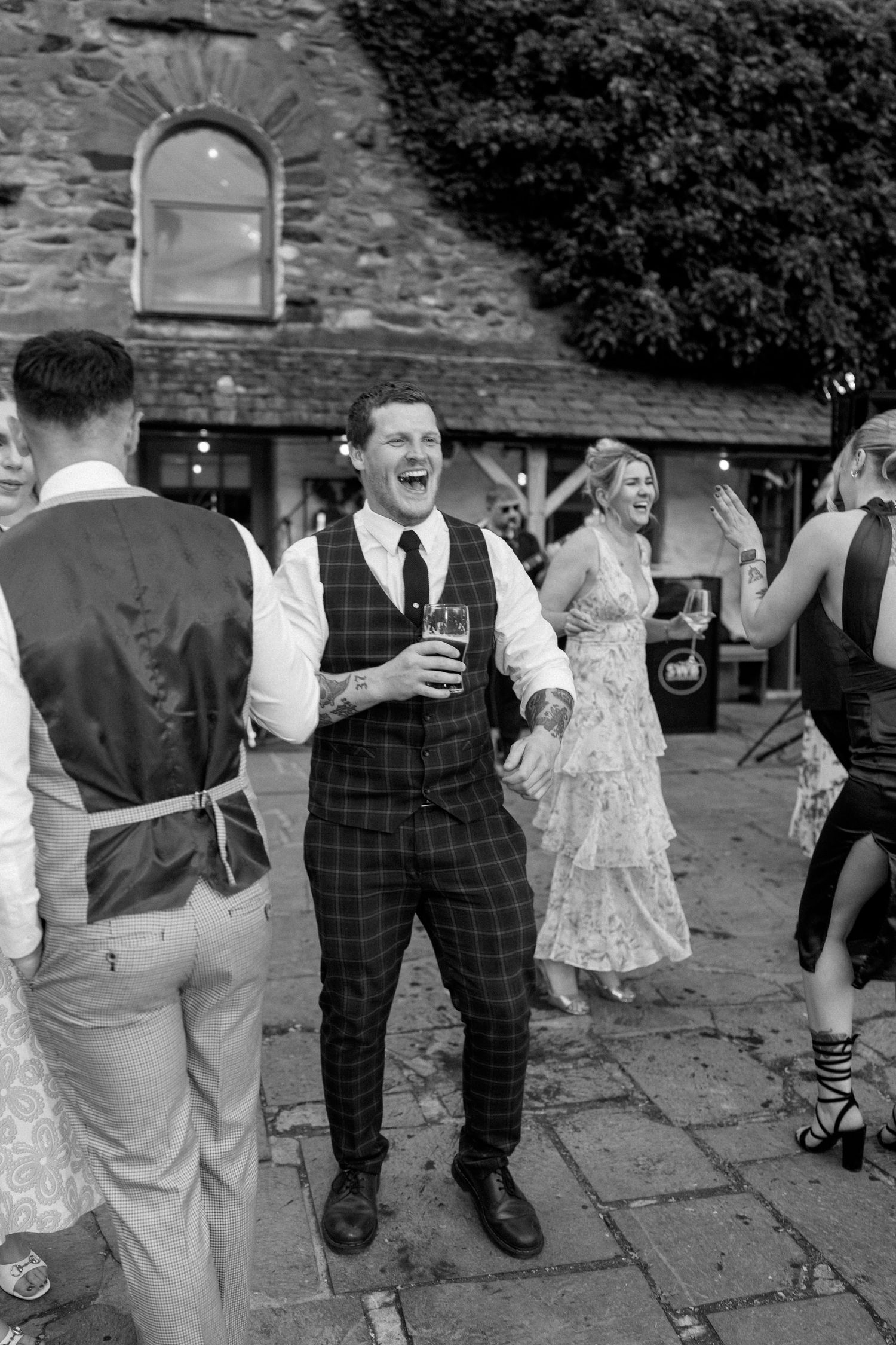 Wedding guests in formal attire socialize and celebrate on outdoor stone patio.