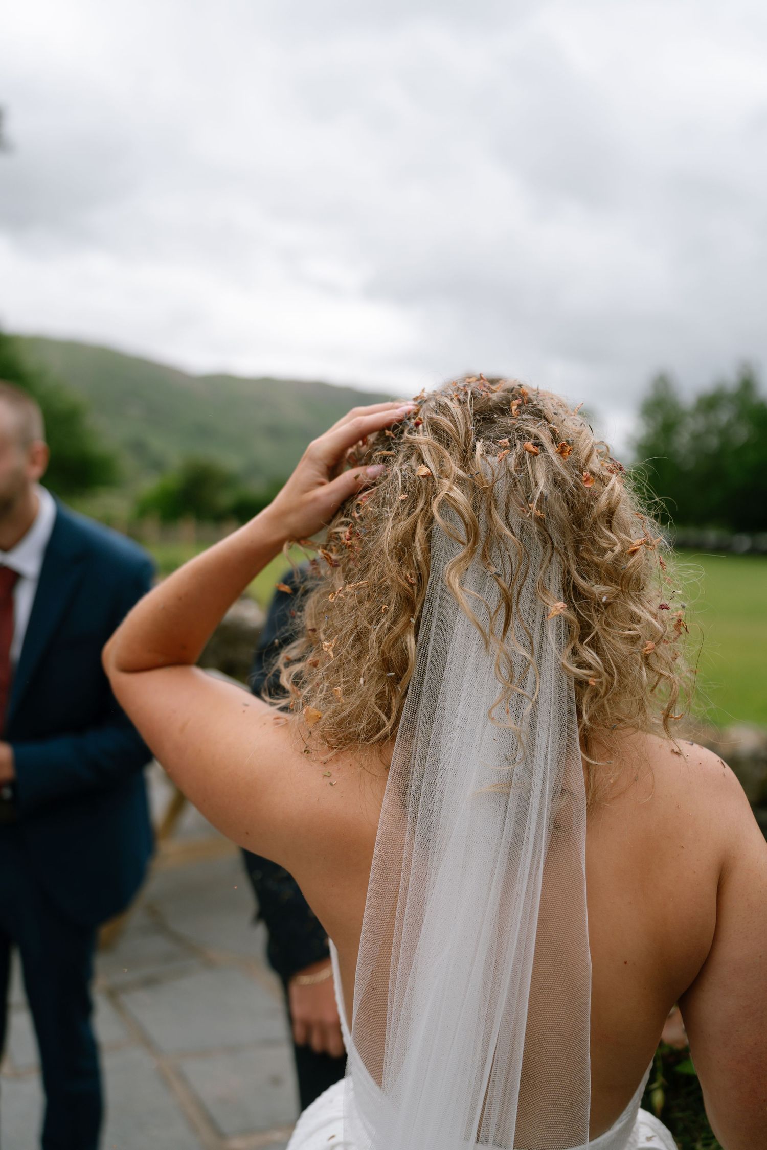 A close-up view of a bridal veil and curly hair against a cloudy mountain backdrop.