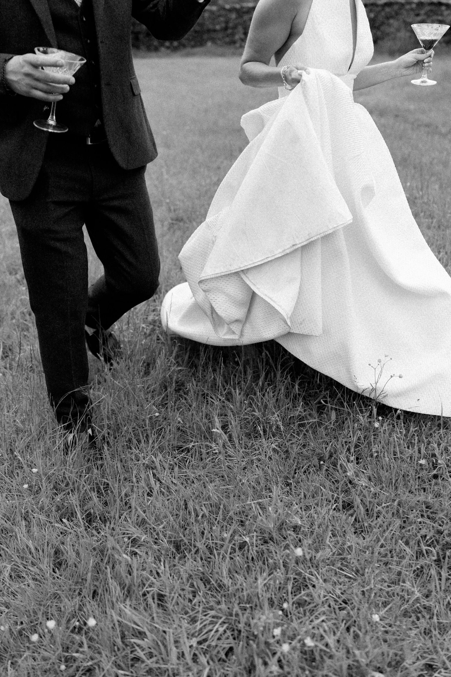 Black and white photo of formal wedding attire with flowing white dress and dark suit on grass.