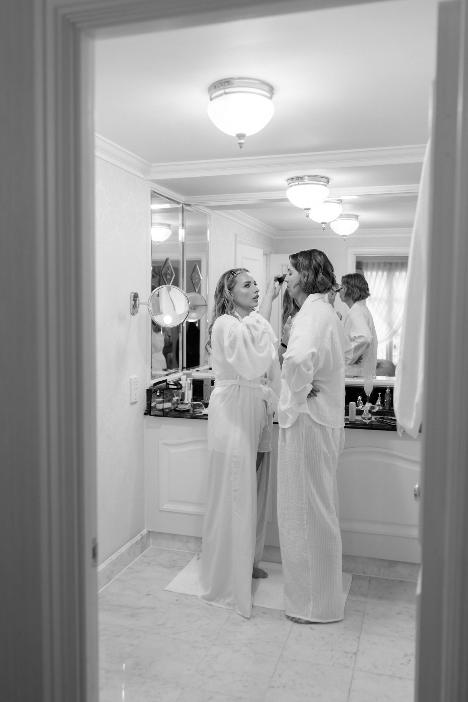 Multiple people in white robes gather in a brightly lit hallway with reflective floors and ceiling lights.