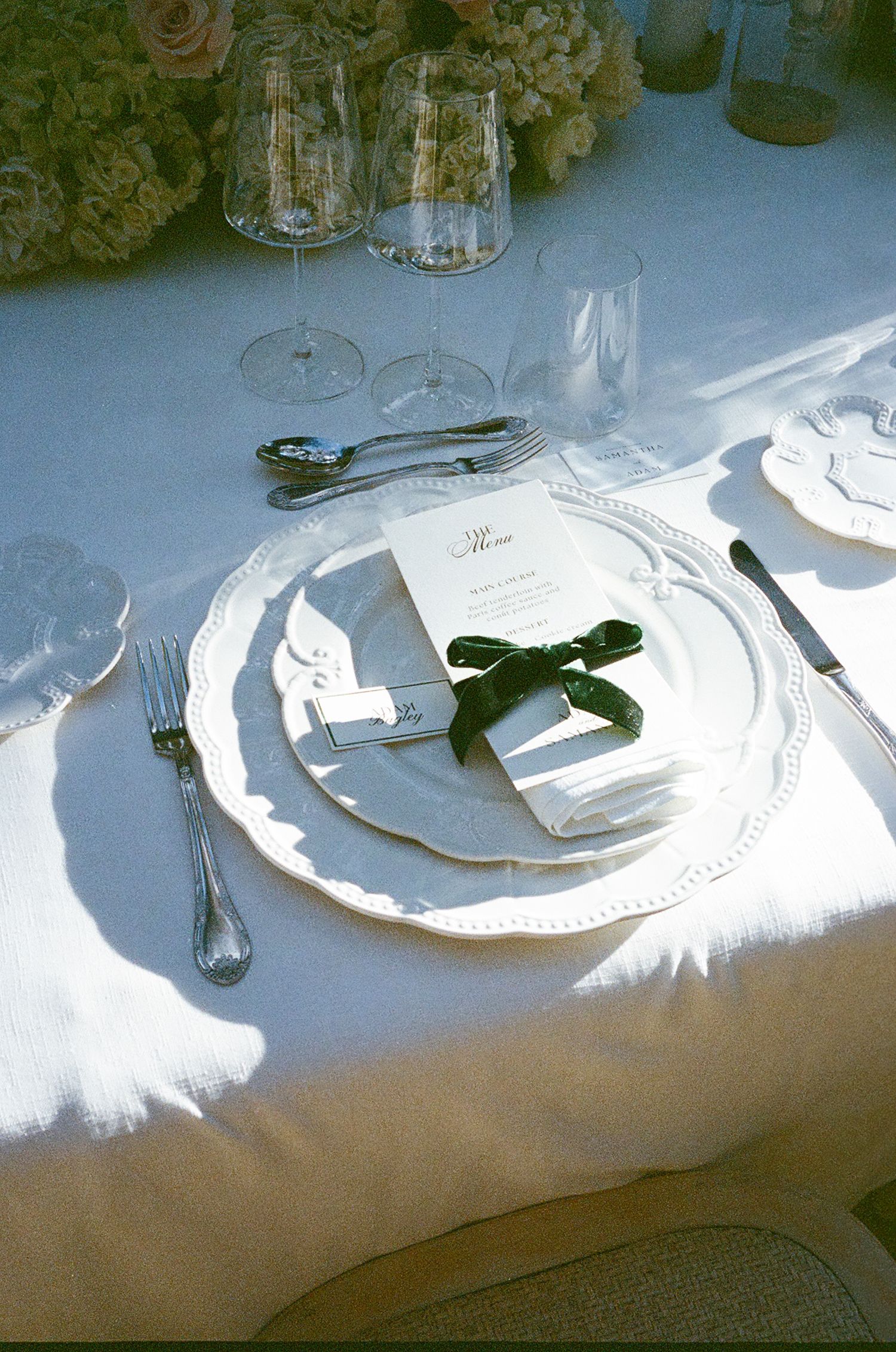 Elegant place settings with white plates and silverware on a light tablecloth cast dramatic shadows in natural light.