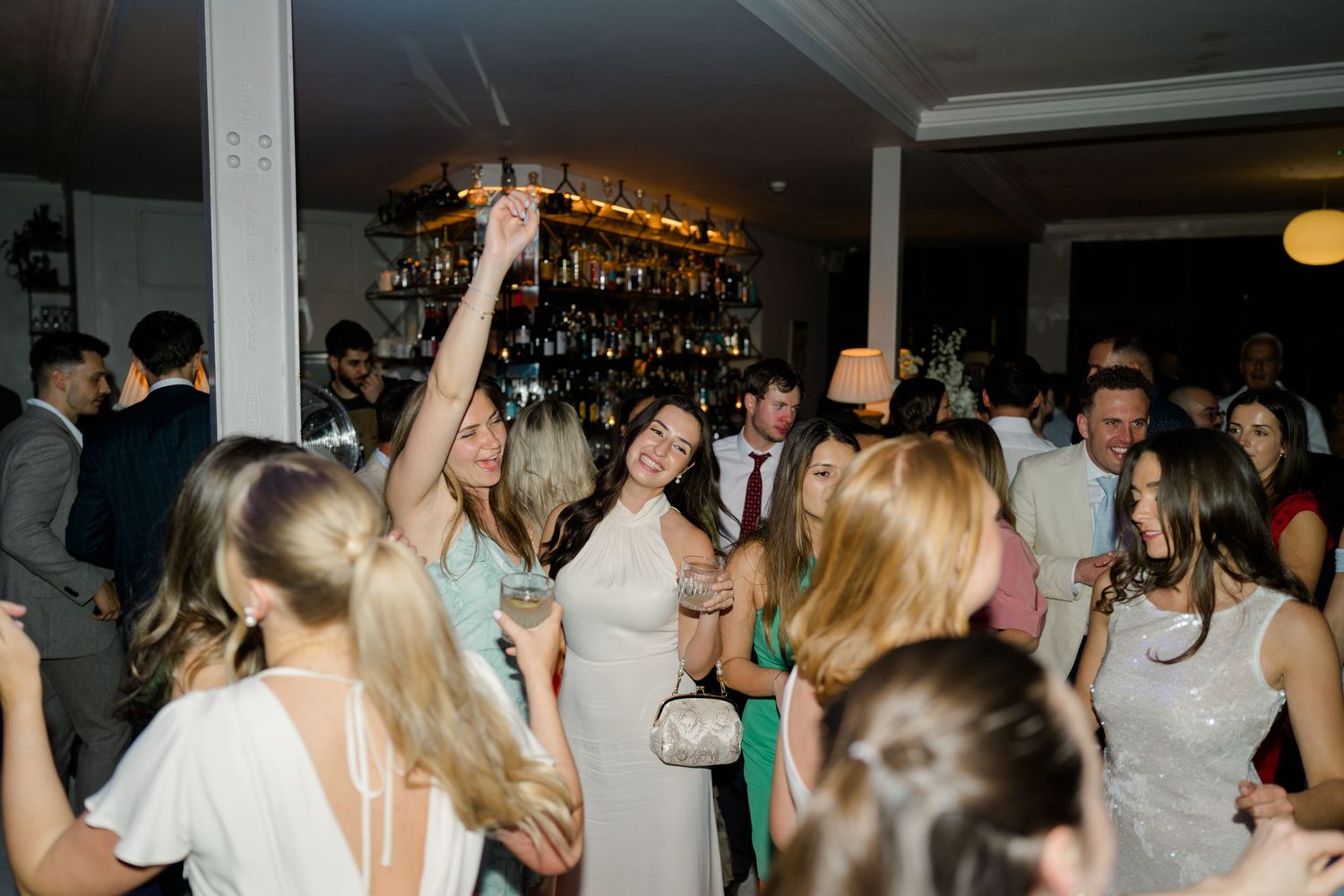 Lively wedding reception dance floor with guests celebrating and bride raising hand with drink.