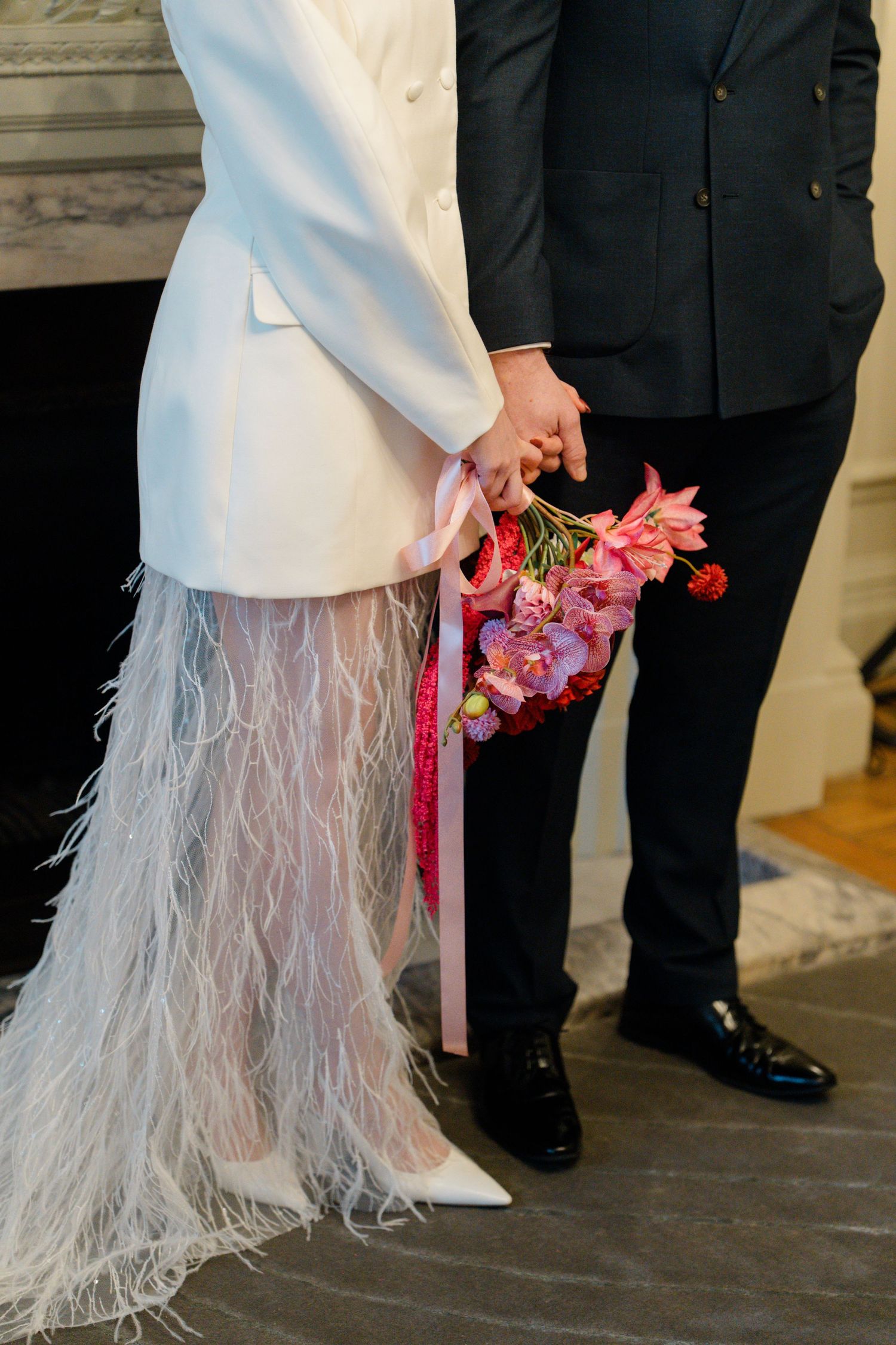 Bride and groom holding hands with pink floral bouquet at wedding ceremony.