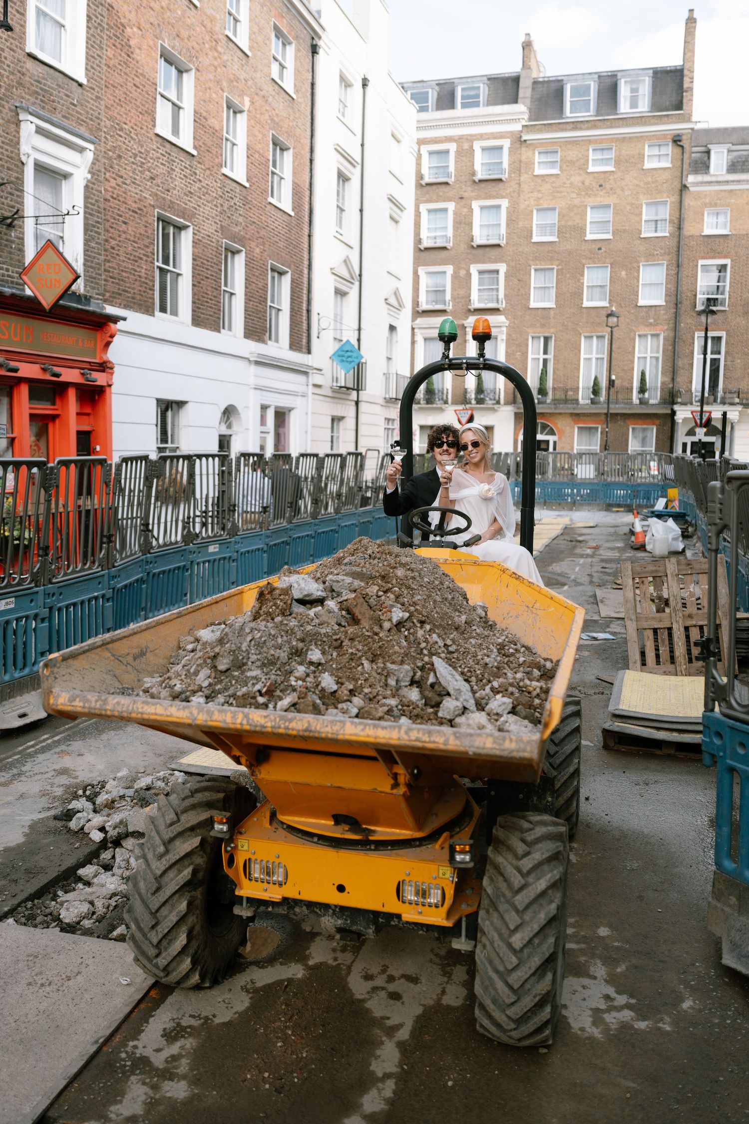 A yellow dump truck loaded with rubble parked on a street surrounded by brick buildings.