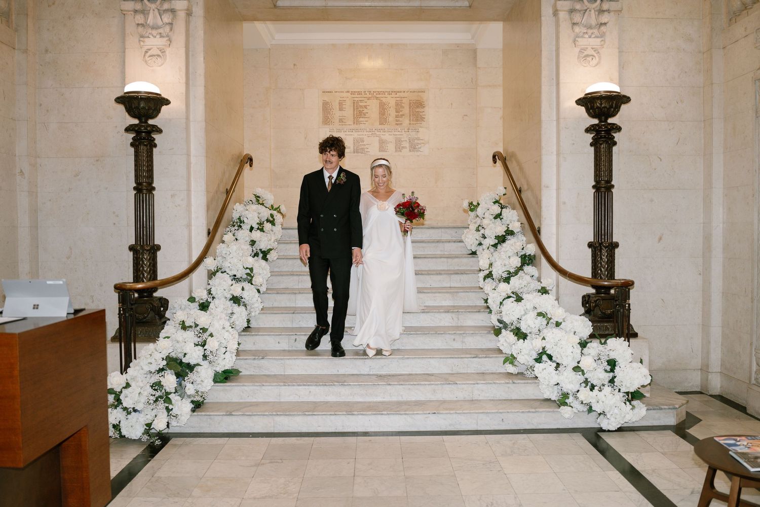 Elegant marble staircase adorned with white floral arrangements and a couple walking down.