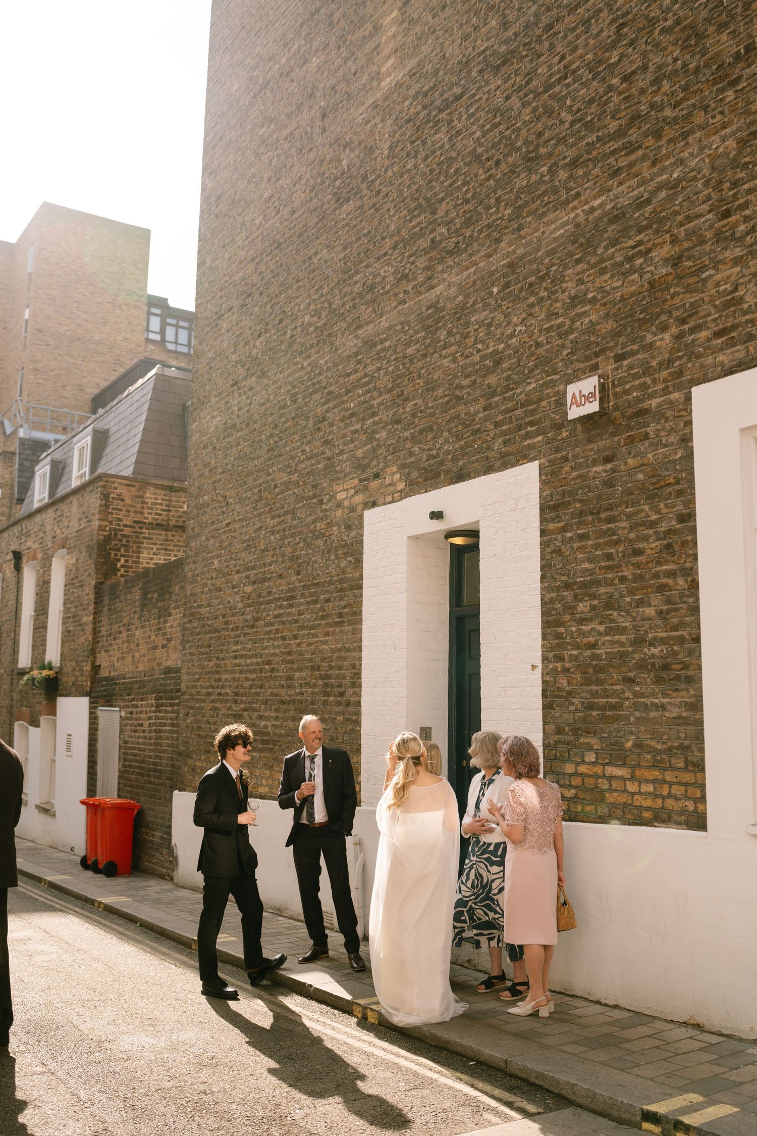 Wedding party gathering in a narrow brick-walled mews street.